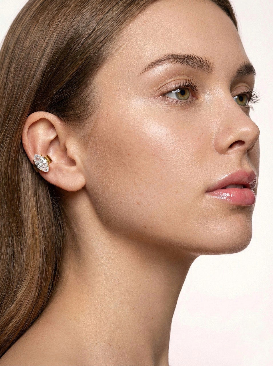 Close-up of a woman wearing a diamond earring on a light background