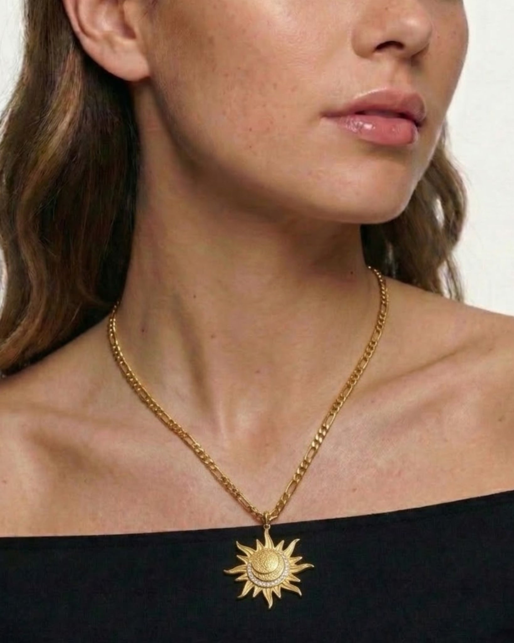 Woman wearing a gold necklace with a sun pendant on a plain background