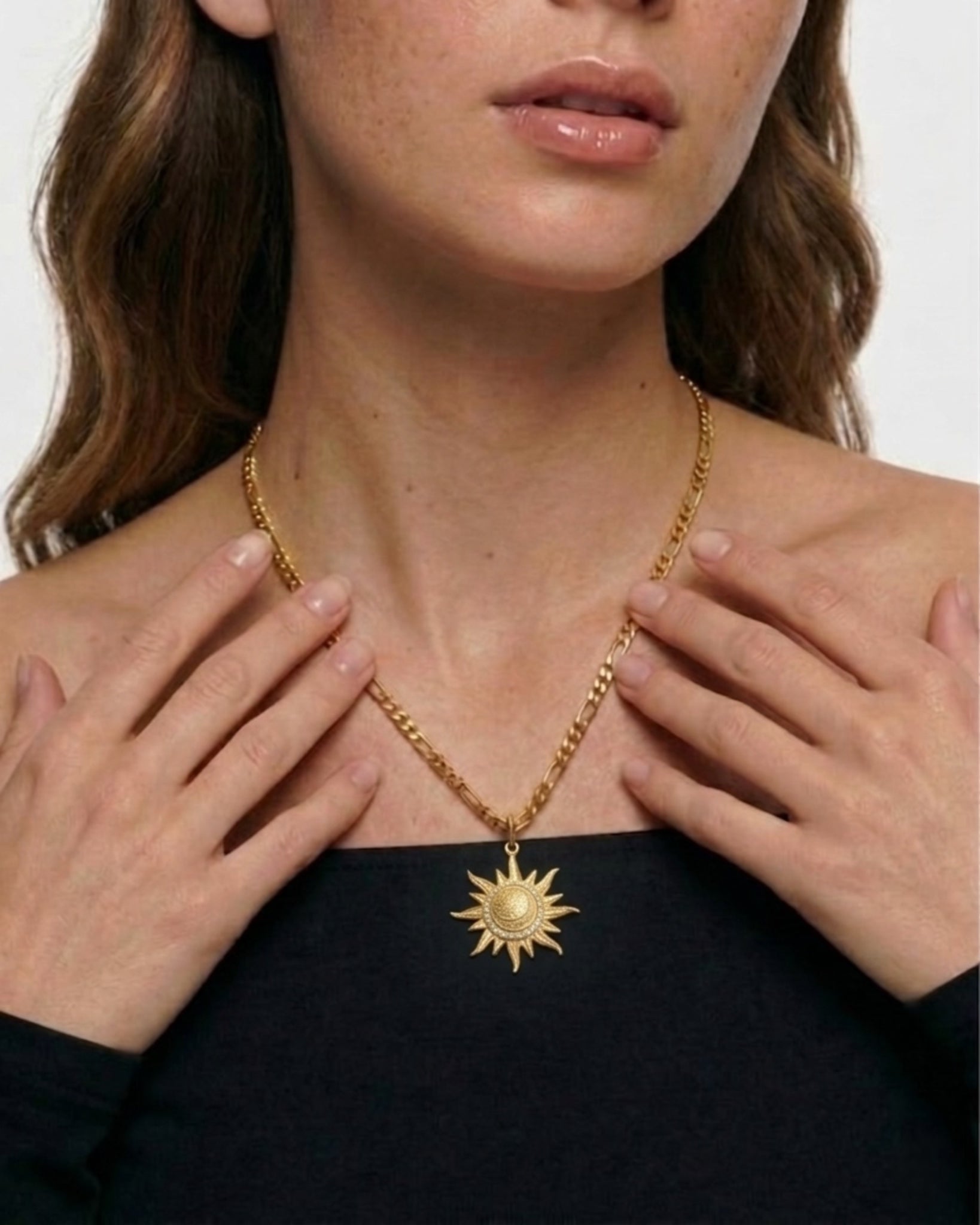 Woman wearing a gold necklace with a sun pendant against a neutral background