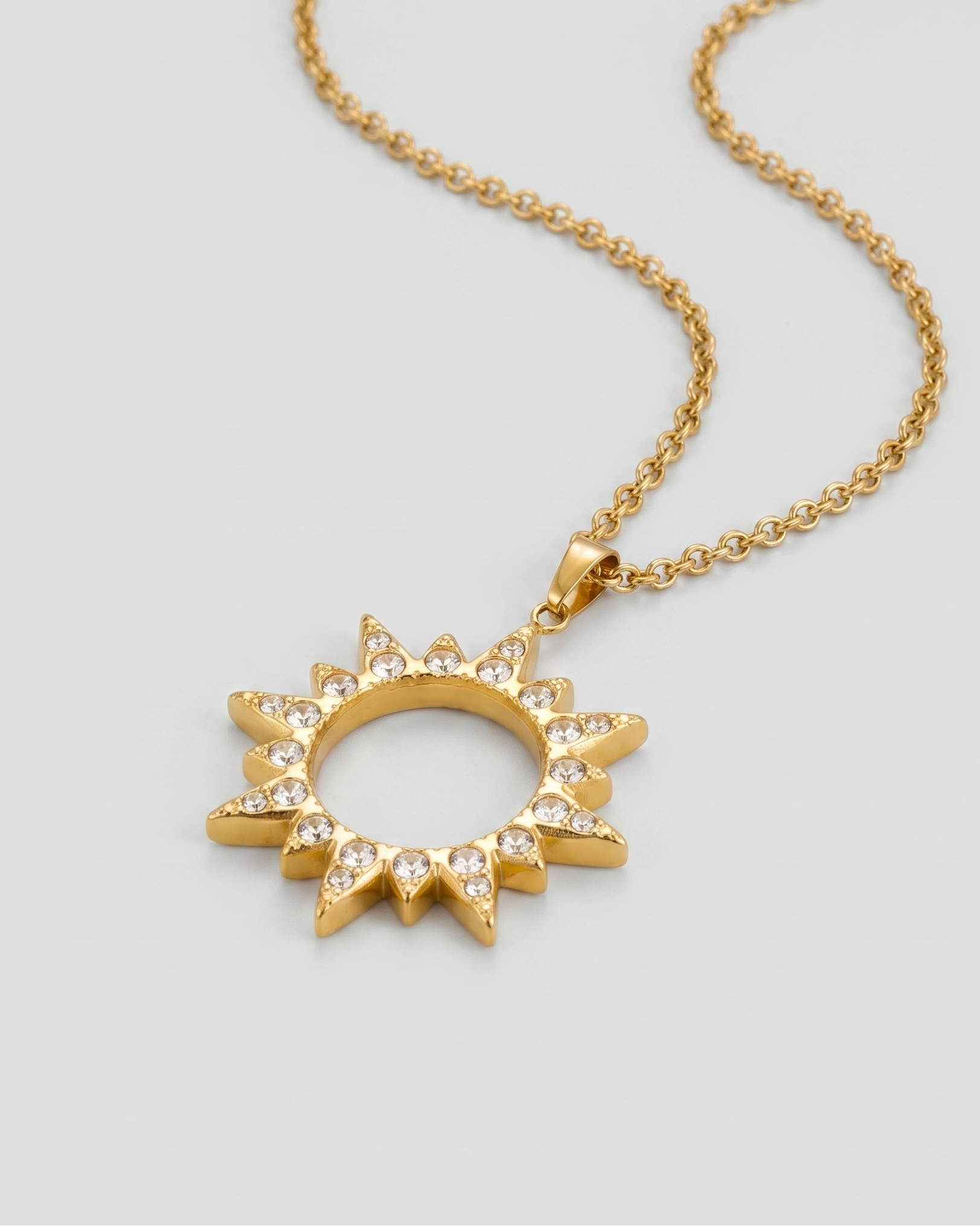 Gold necklace with a sun-shaped pendant on a light gray background