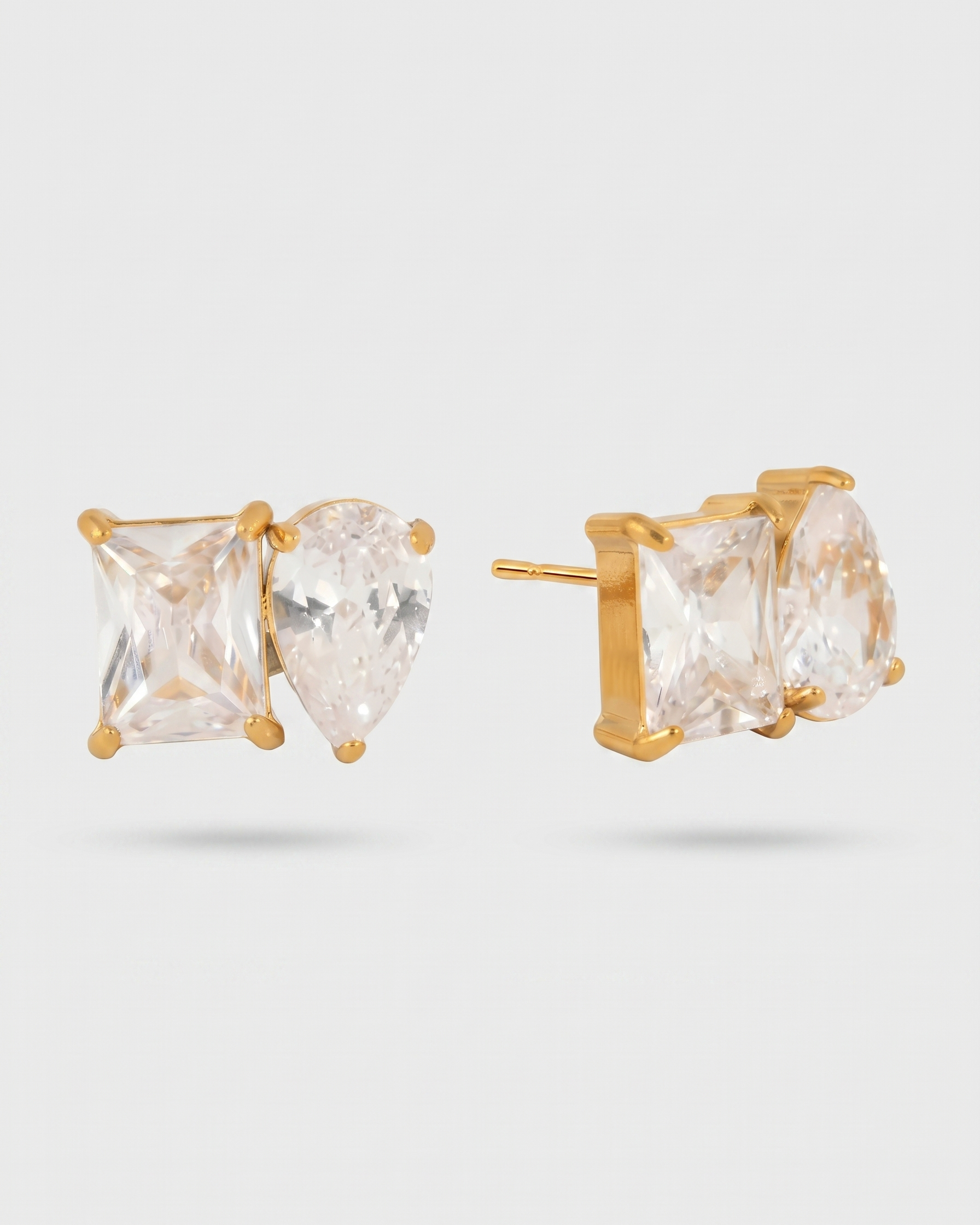 Gold stud earrings with clear gemstones on a light gray background