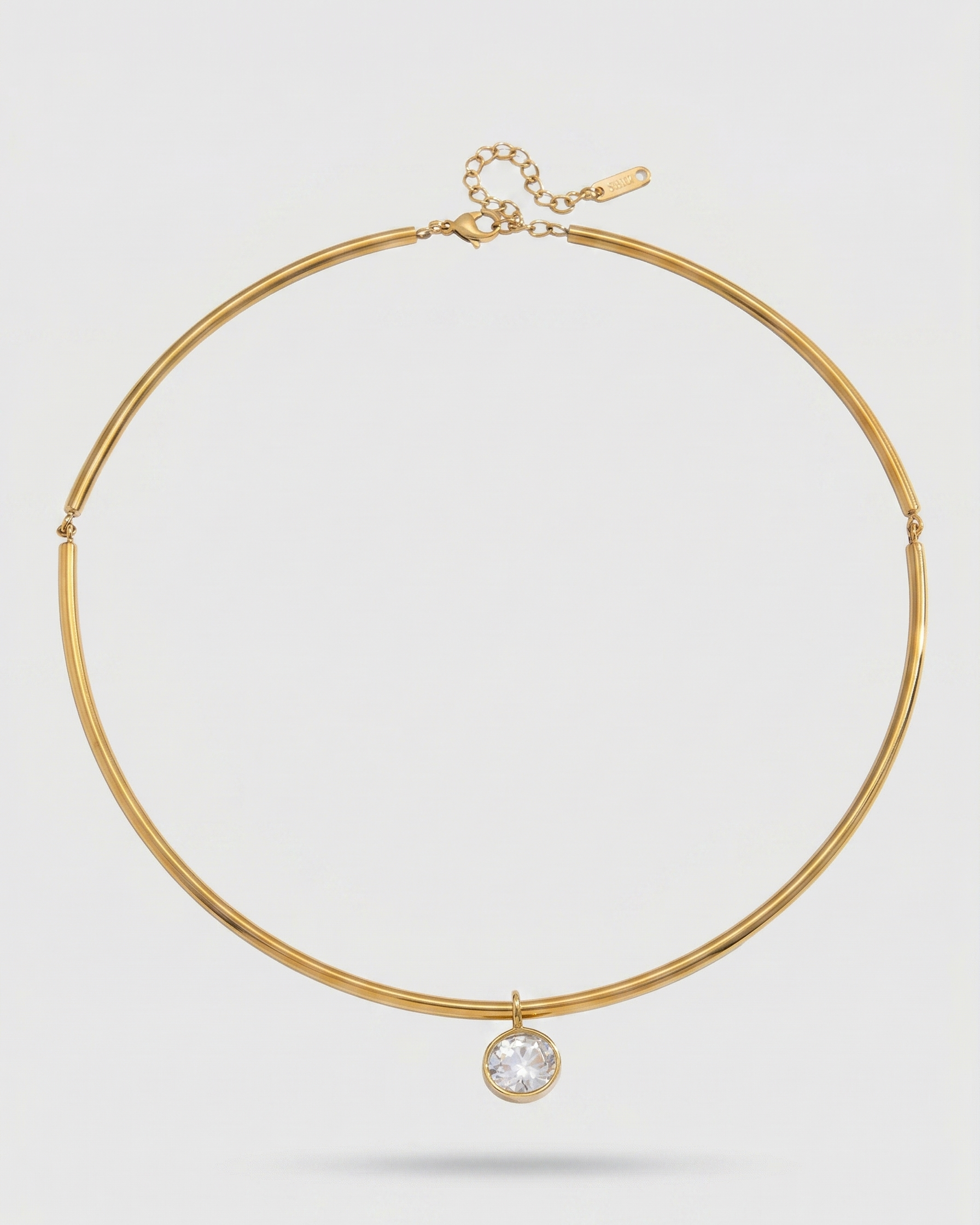 Gold necklace with a clear gemstone on a light gray background
