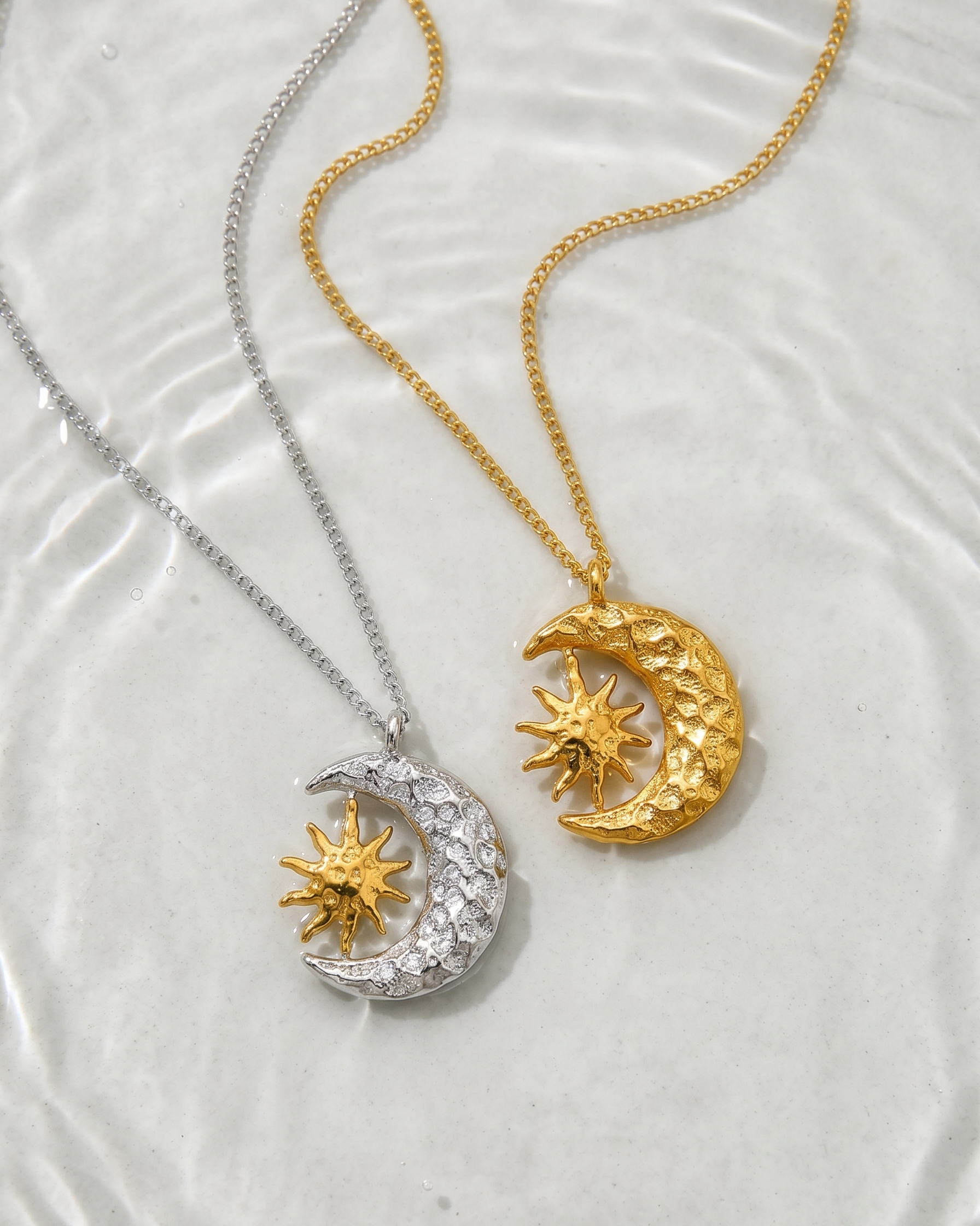 Two necklaces with moon and star pendants on a textured white surface
