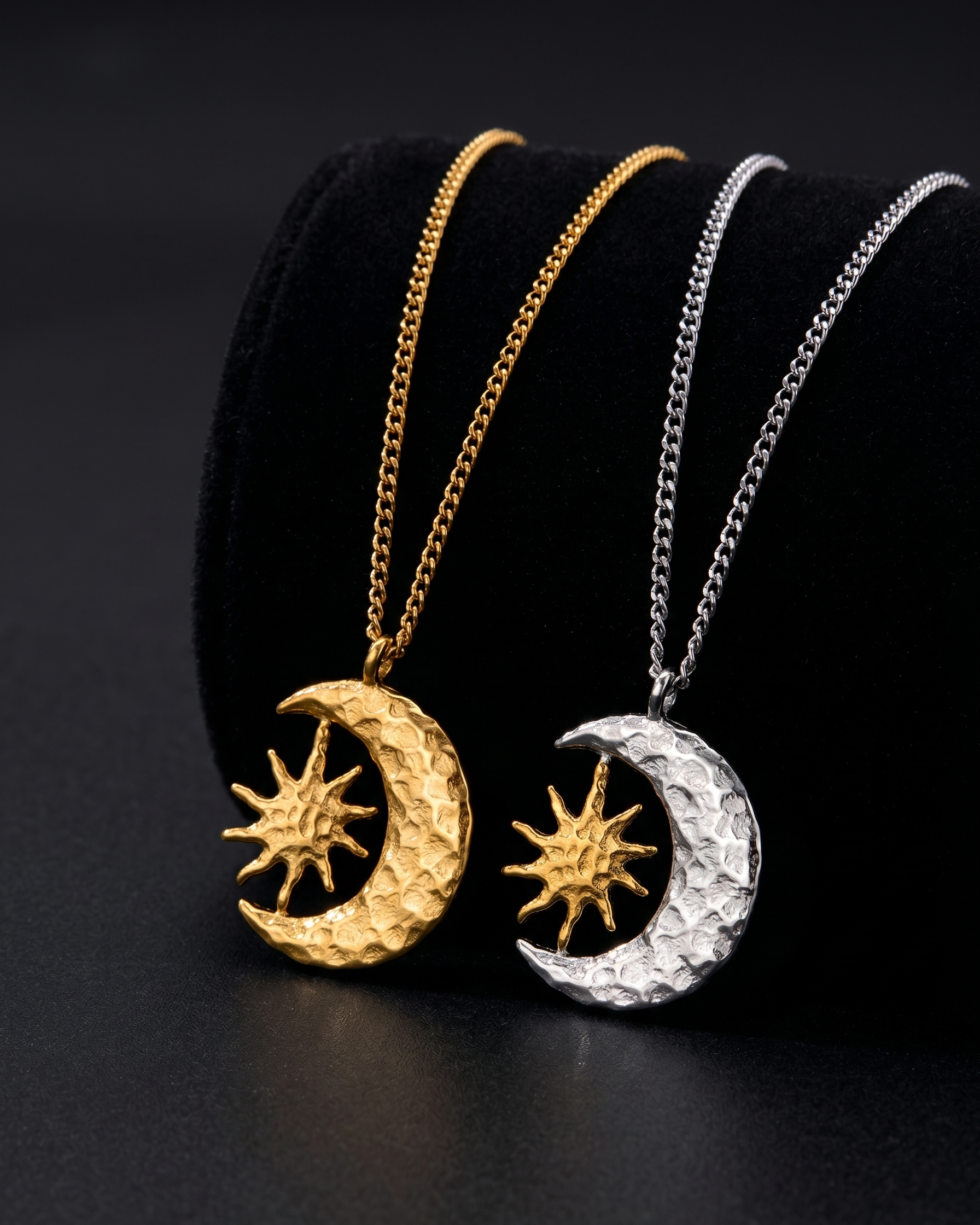 Two moon and sun pendants on gold and silver chains against a black background
