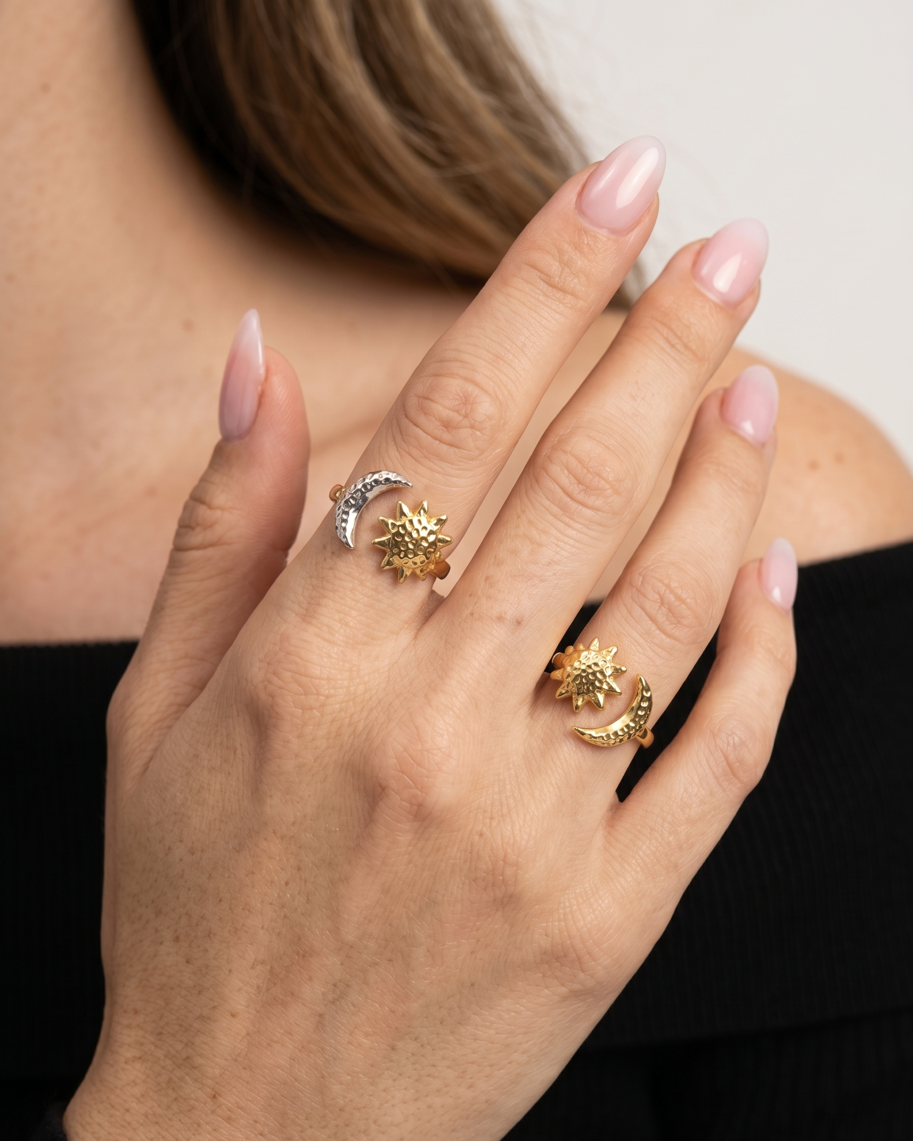 Hand wearing two rings with star and moon designs on a neutral background