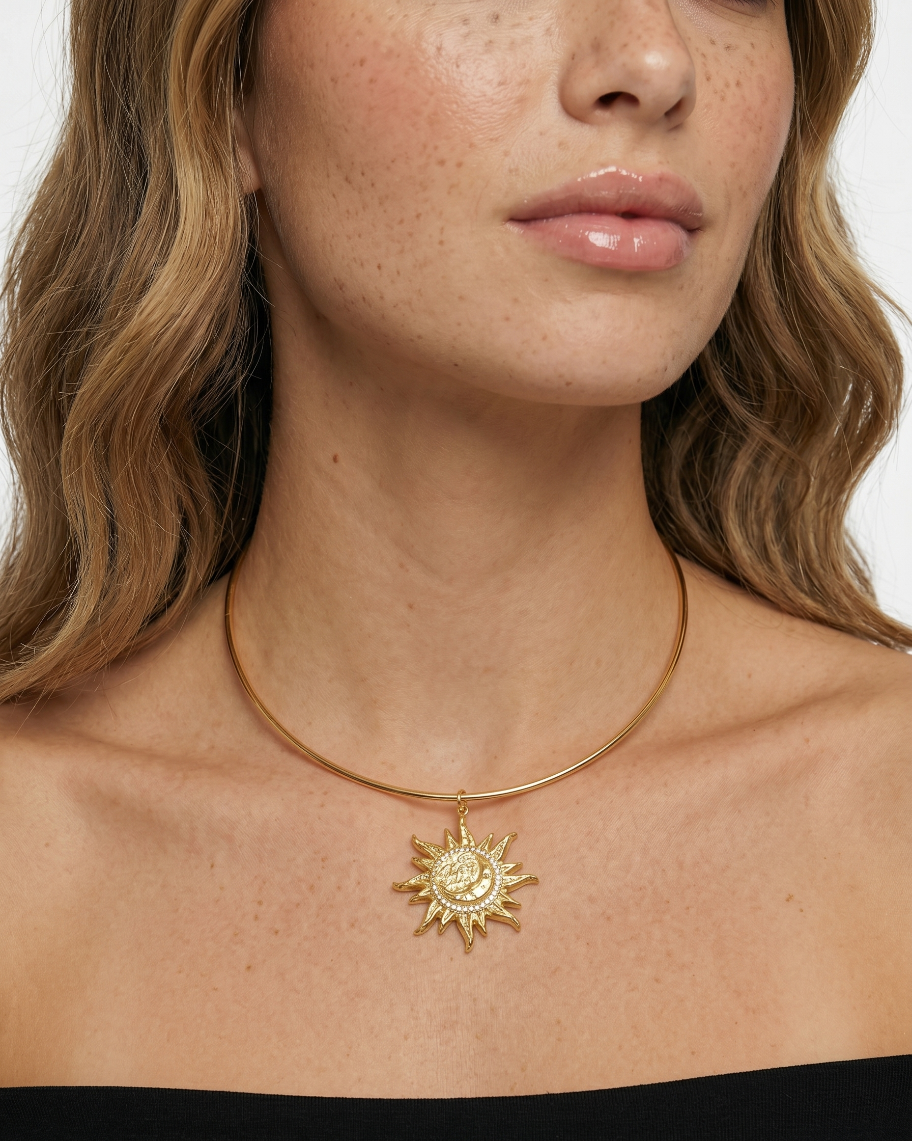 Close-up of a woman wearing a gold necklace with a sun pendant on a plain background