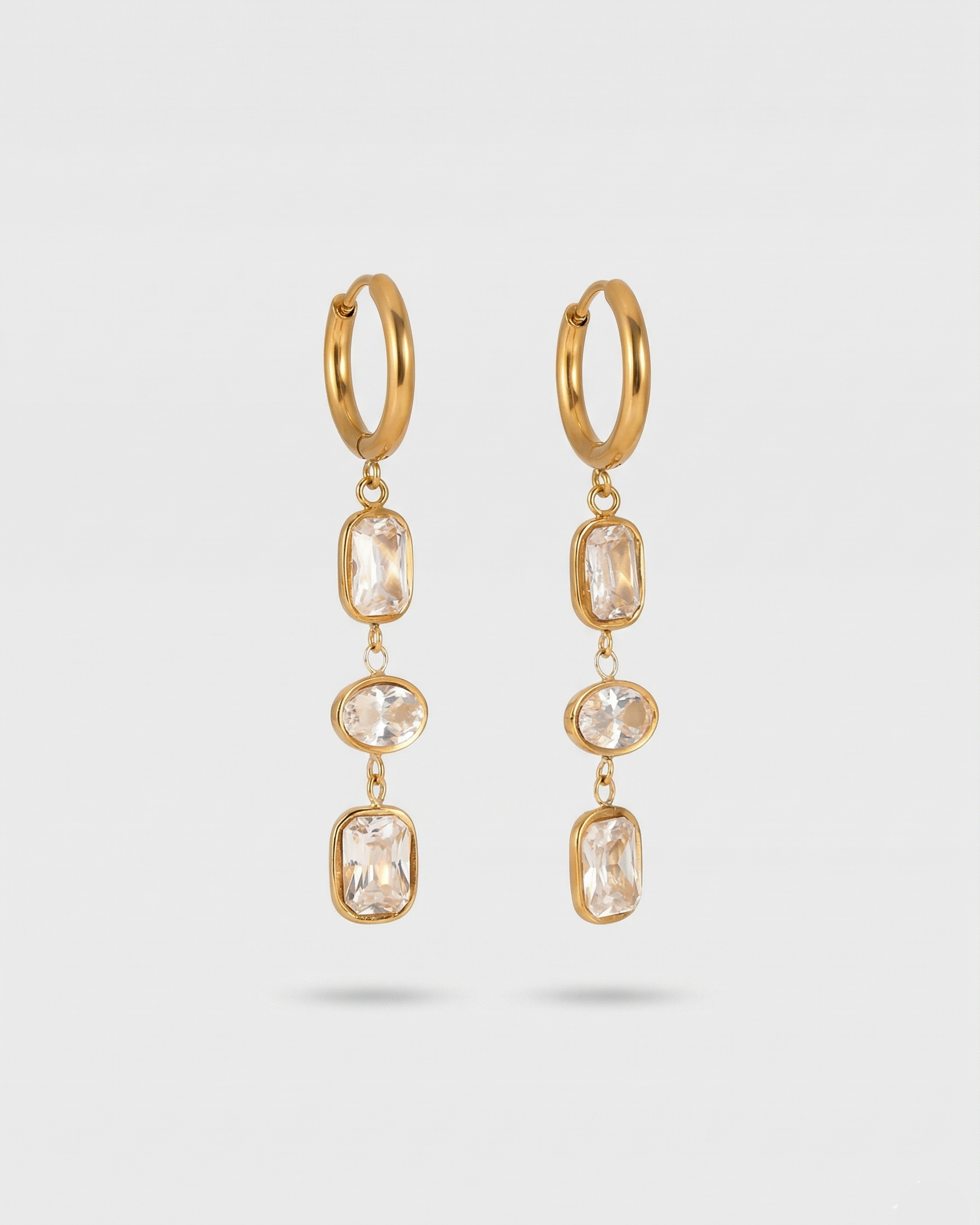 Gold hoop earrings with clear gemstones on a light gray background