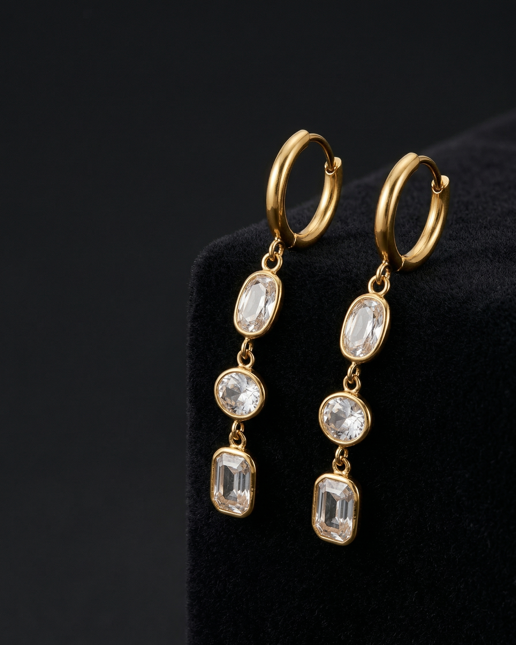 Gold hoop earrings with gemstone drops on a black background