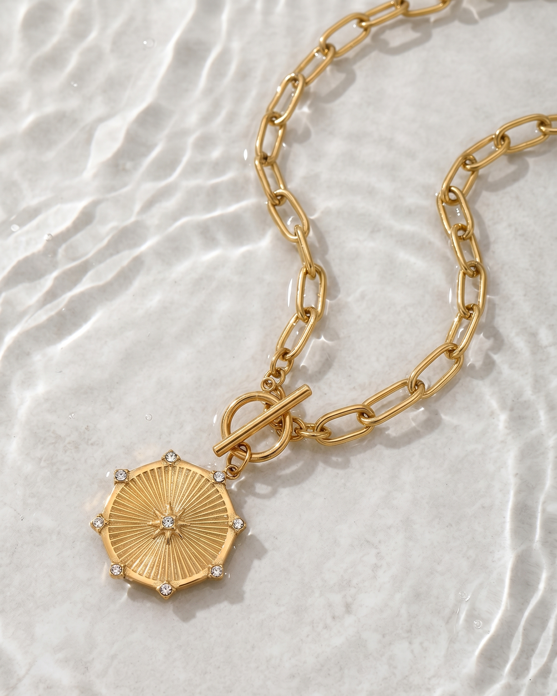Gold chain necklace with a decorative pendant on a textured white background