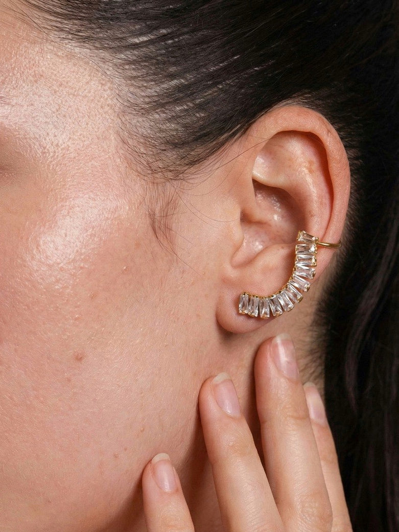Close-up of an ear wearing a gold hoop earring with clear stones, hand touching the earlobe.