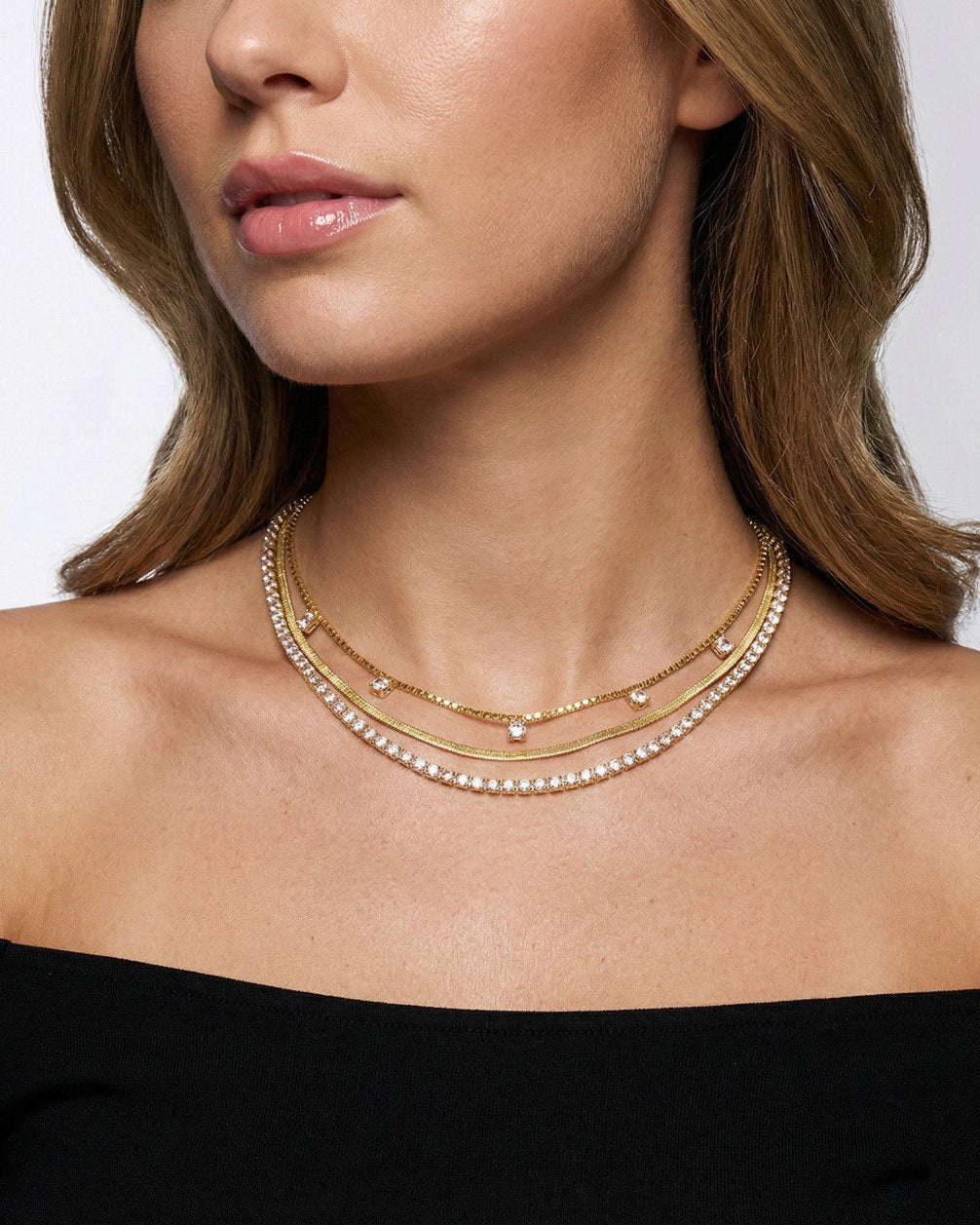 Close-up of a woman wearing a gold necklace with a plain background