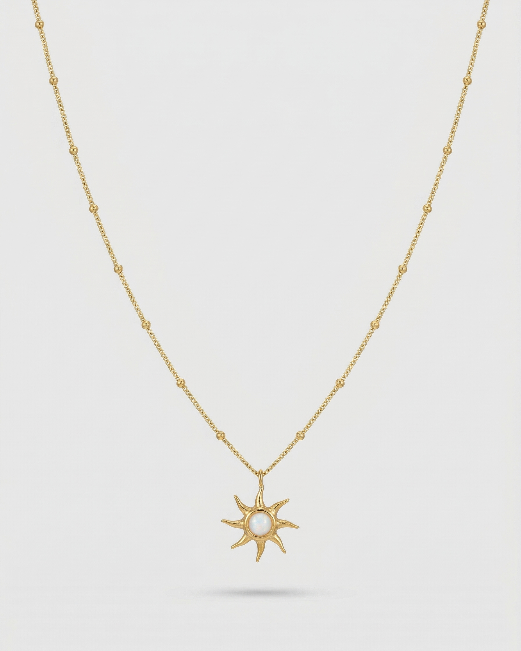 Gold necklace with a sun-shaped pendant on a light gray background