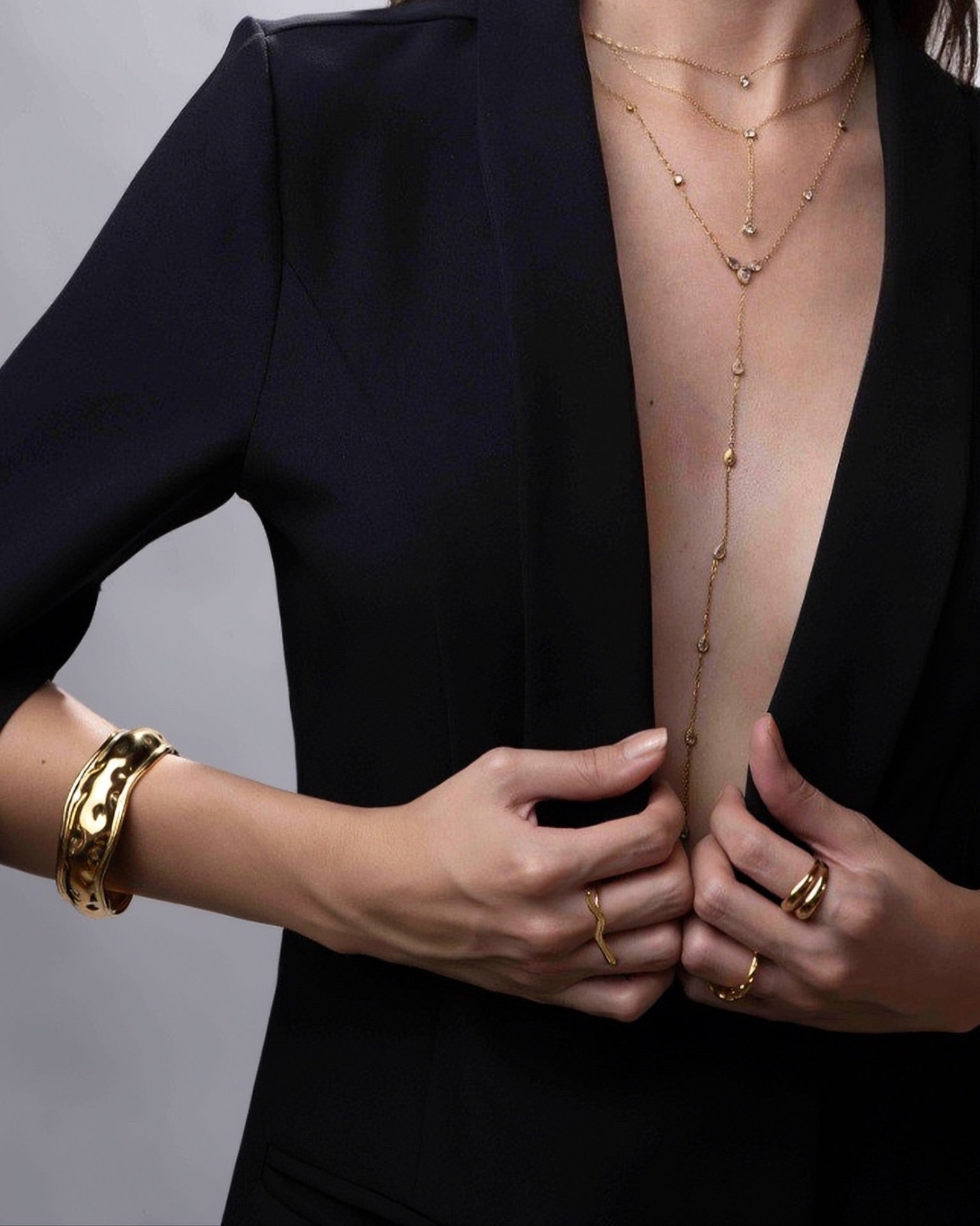 Person wearing gold jewelry including a necklace, bracelet, and rings on a plain background