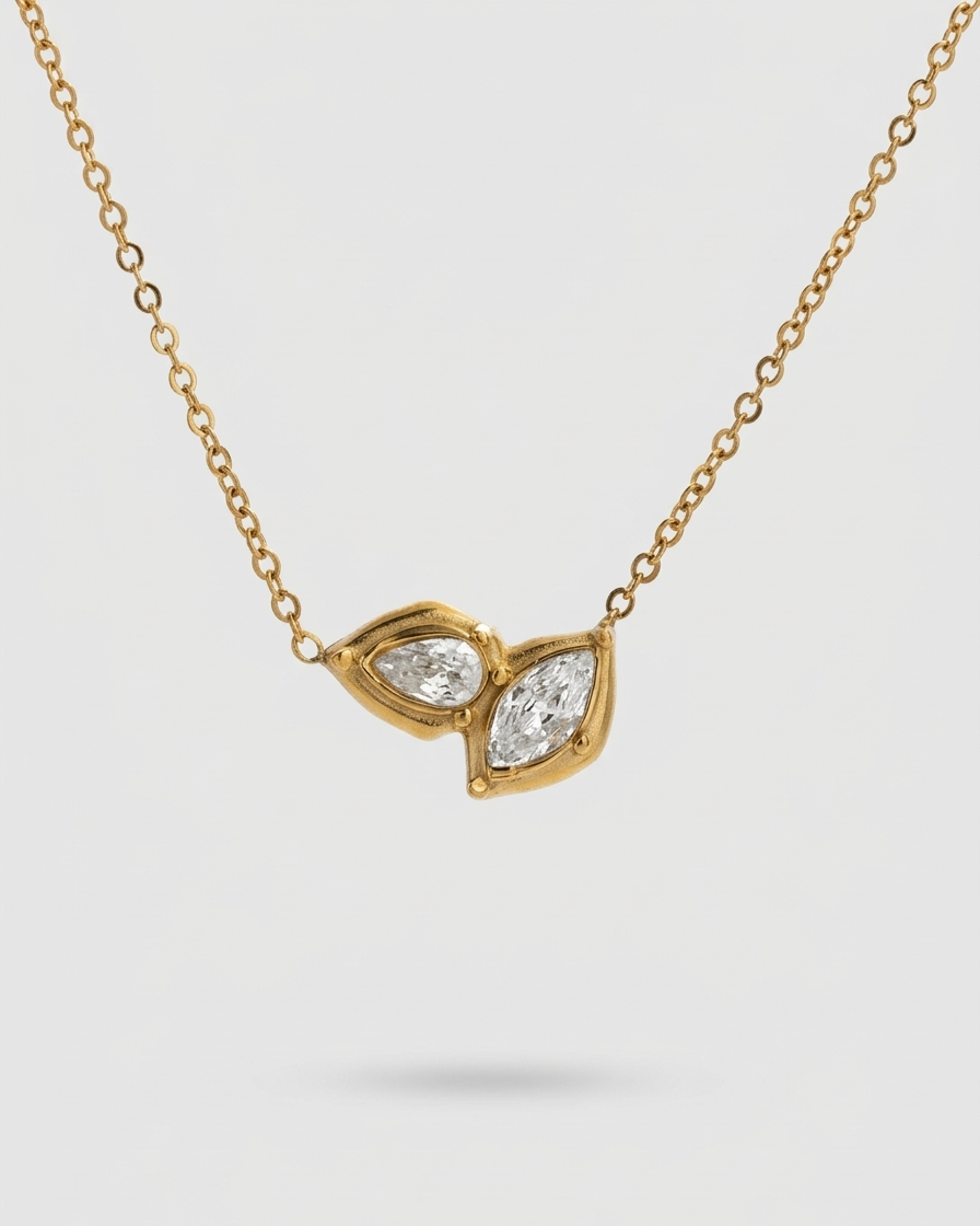 Gold necklace with a leaf-shaped pendant featuring two diamonds on a light gray background