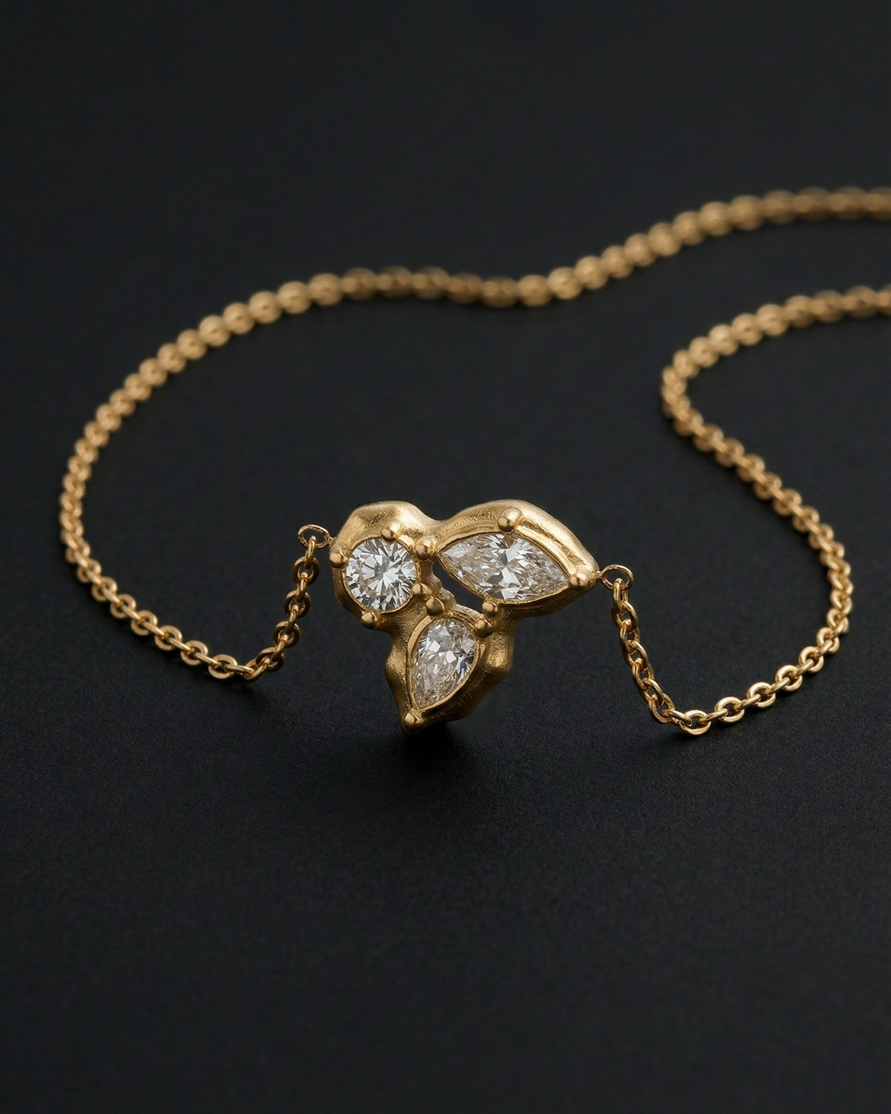 Gold necklace with a leaf-shaped diamond pendant on a dark background