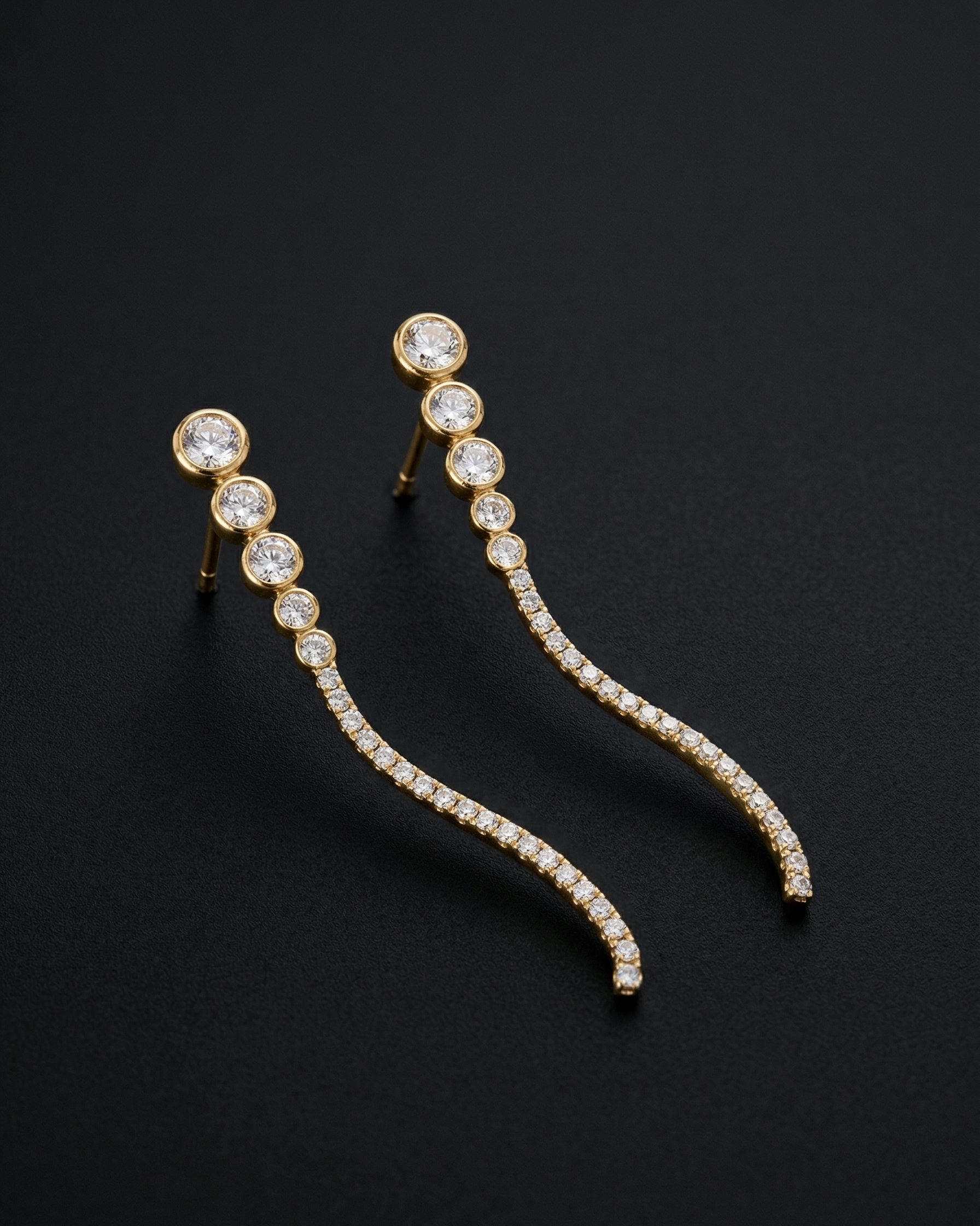 Pair of gold earrings with clear gemstones on a black background