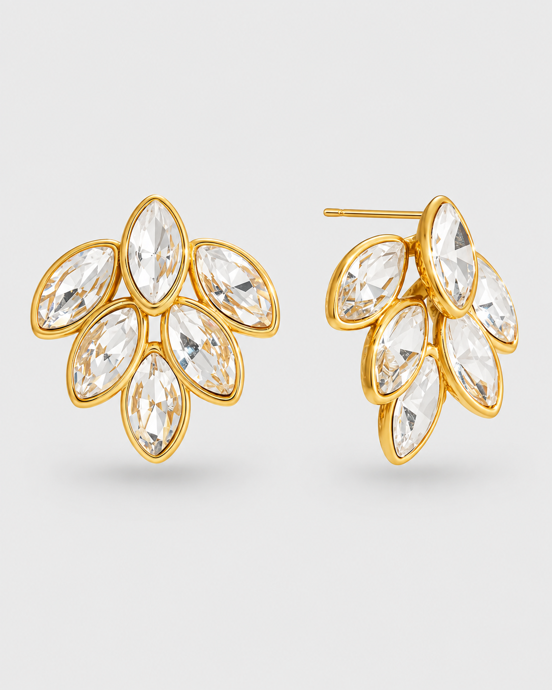 A pair of gold leaf-shaped stud earrings with marquise-cut clear crystals, displayed on a light gray background.