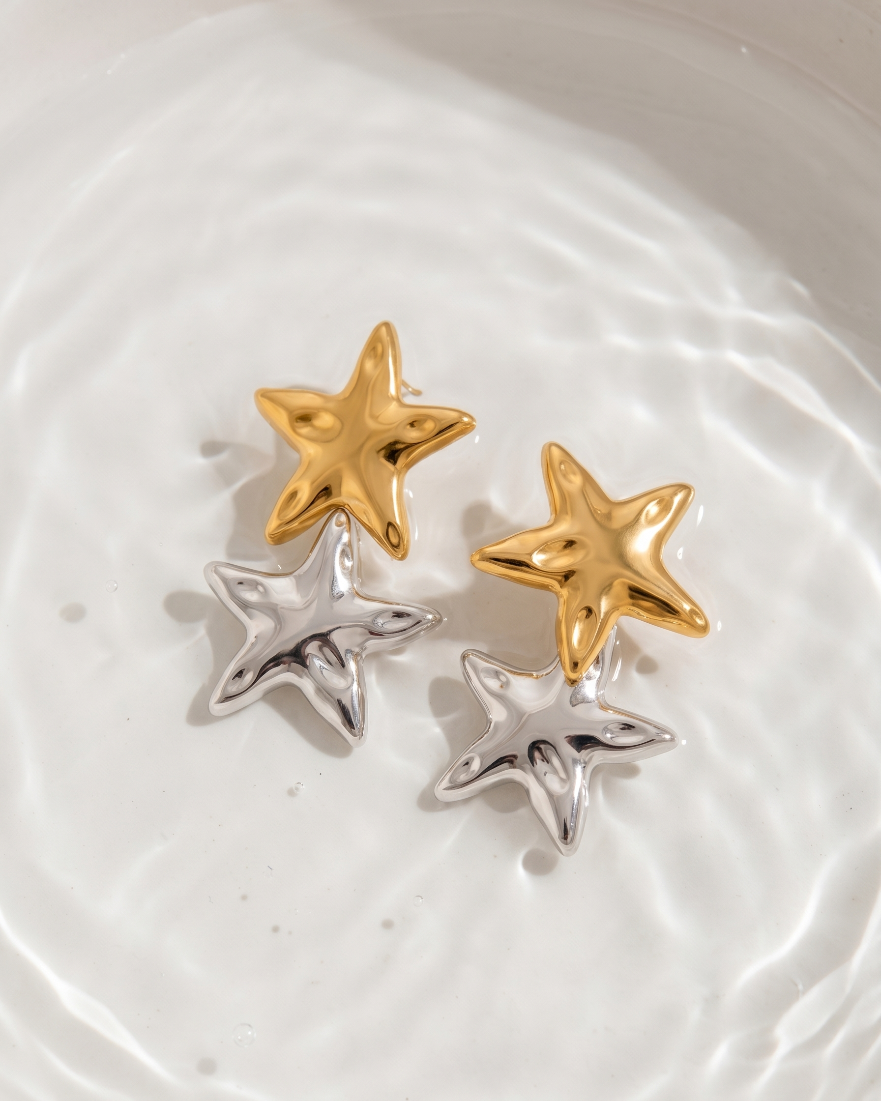 Star-shaped earrings in gold and silver on a white textured surface