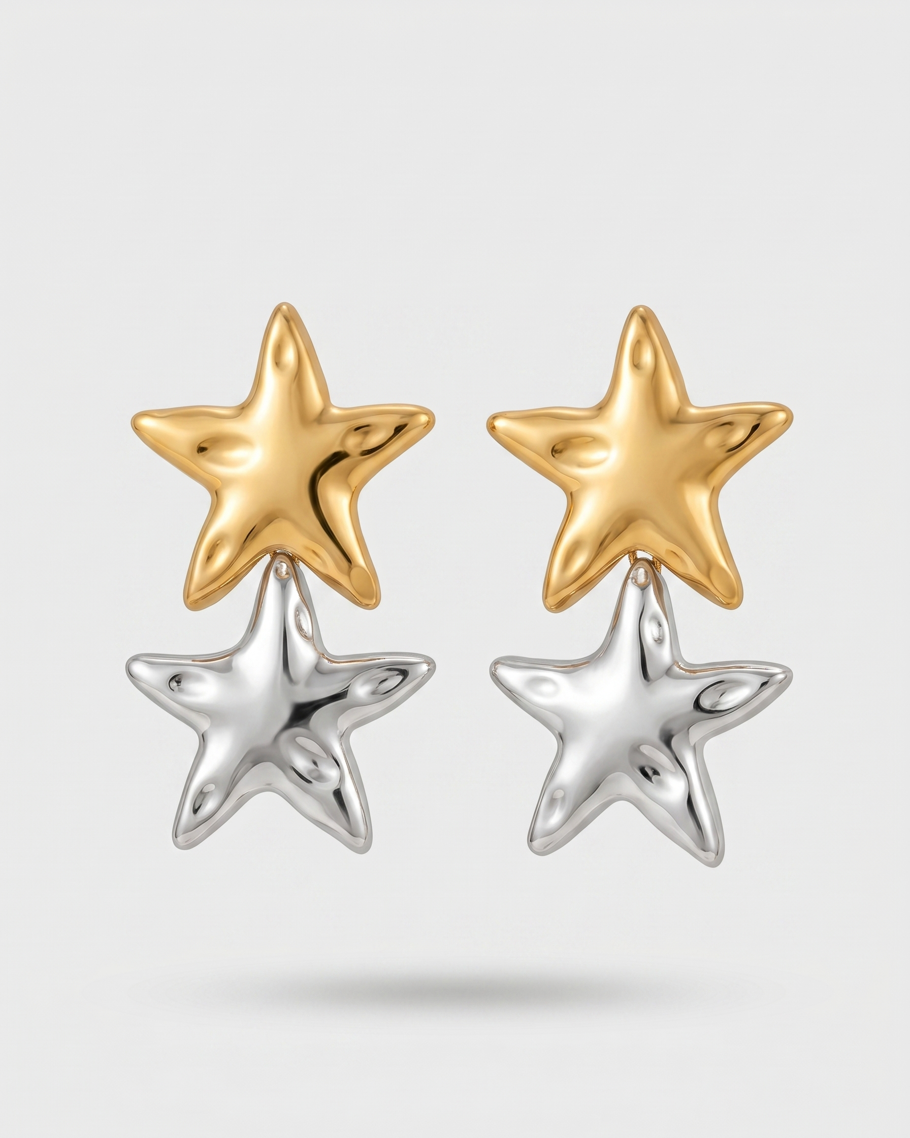 Pair of star-shaped earrings, one gold and one silver, on a light gray background.