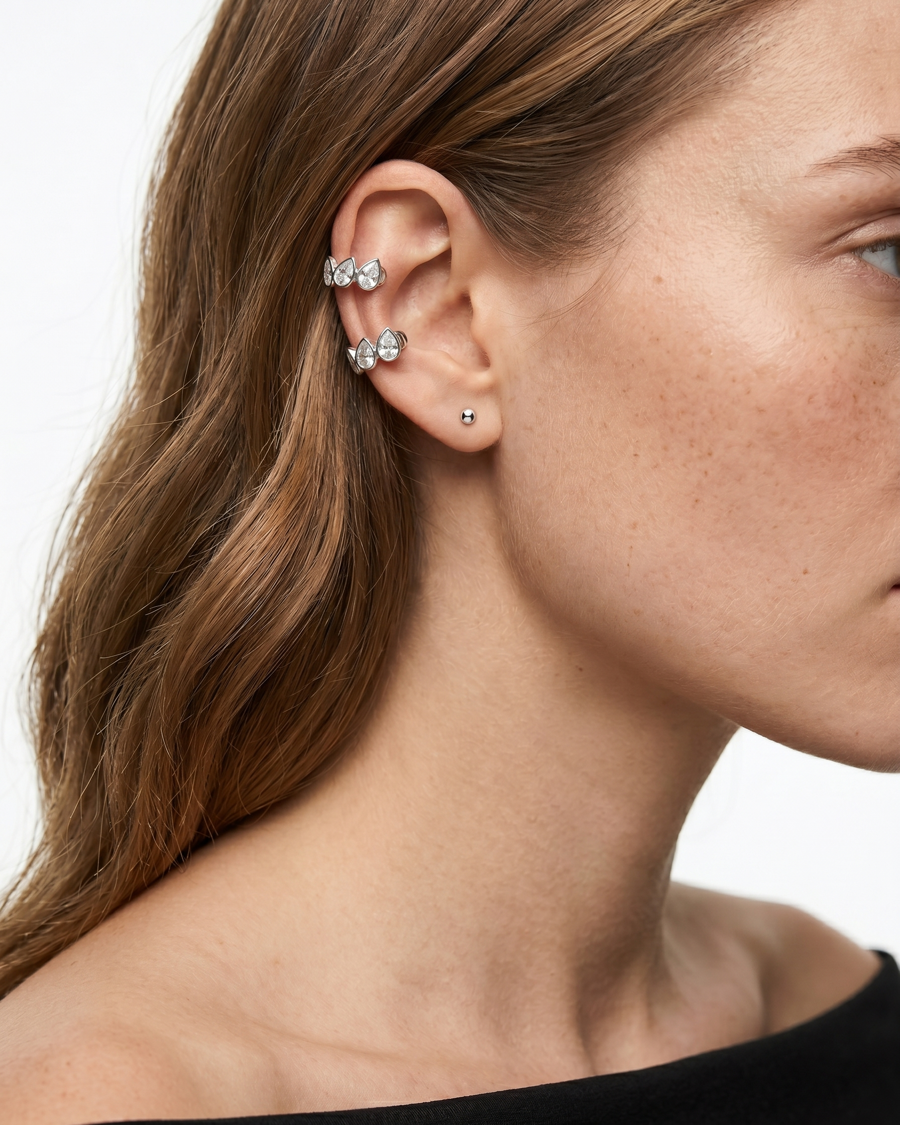 Close-up of a woman's ear wearing multiple earrings with a plain background