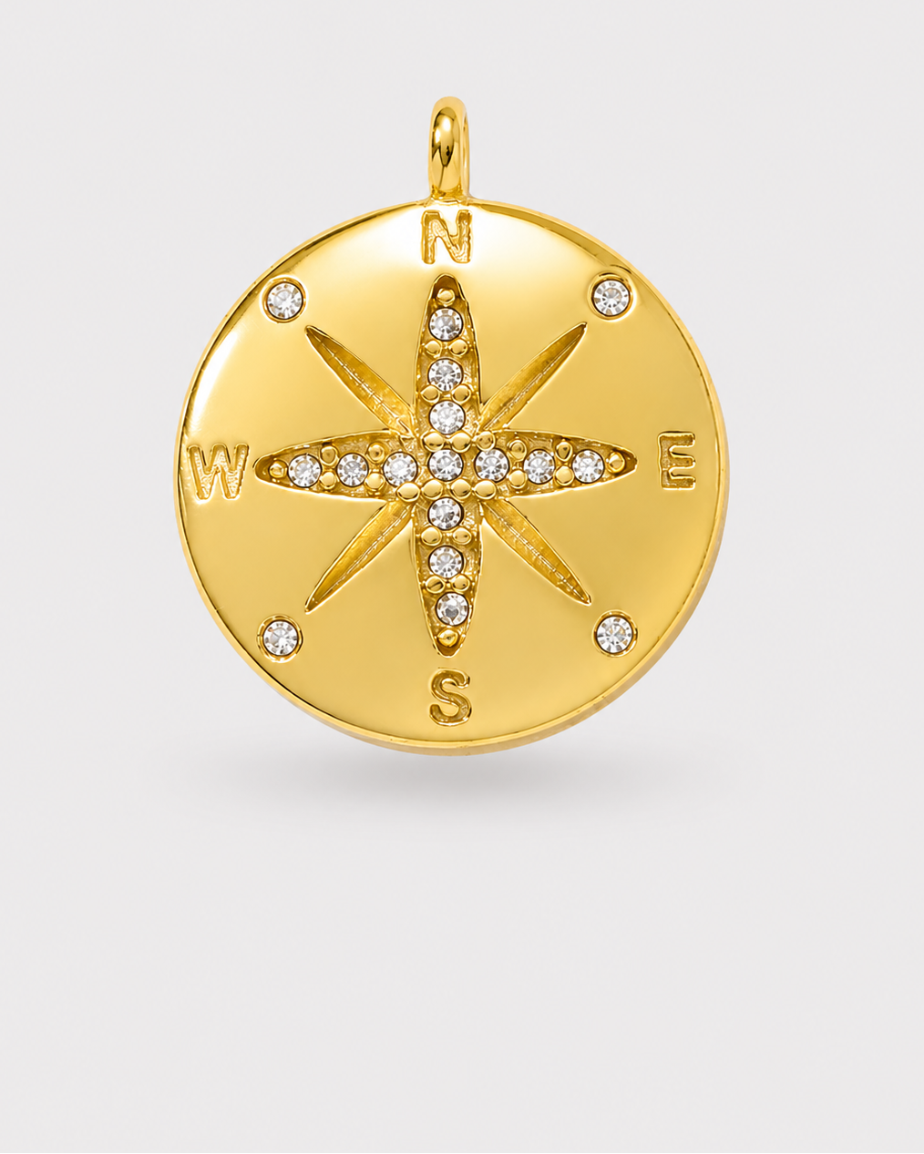 A round gold compass pendant charm featuring a star design set with small clear stones and engraved cardinal directions N, S, E, W on a light gray background.