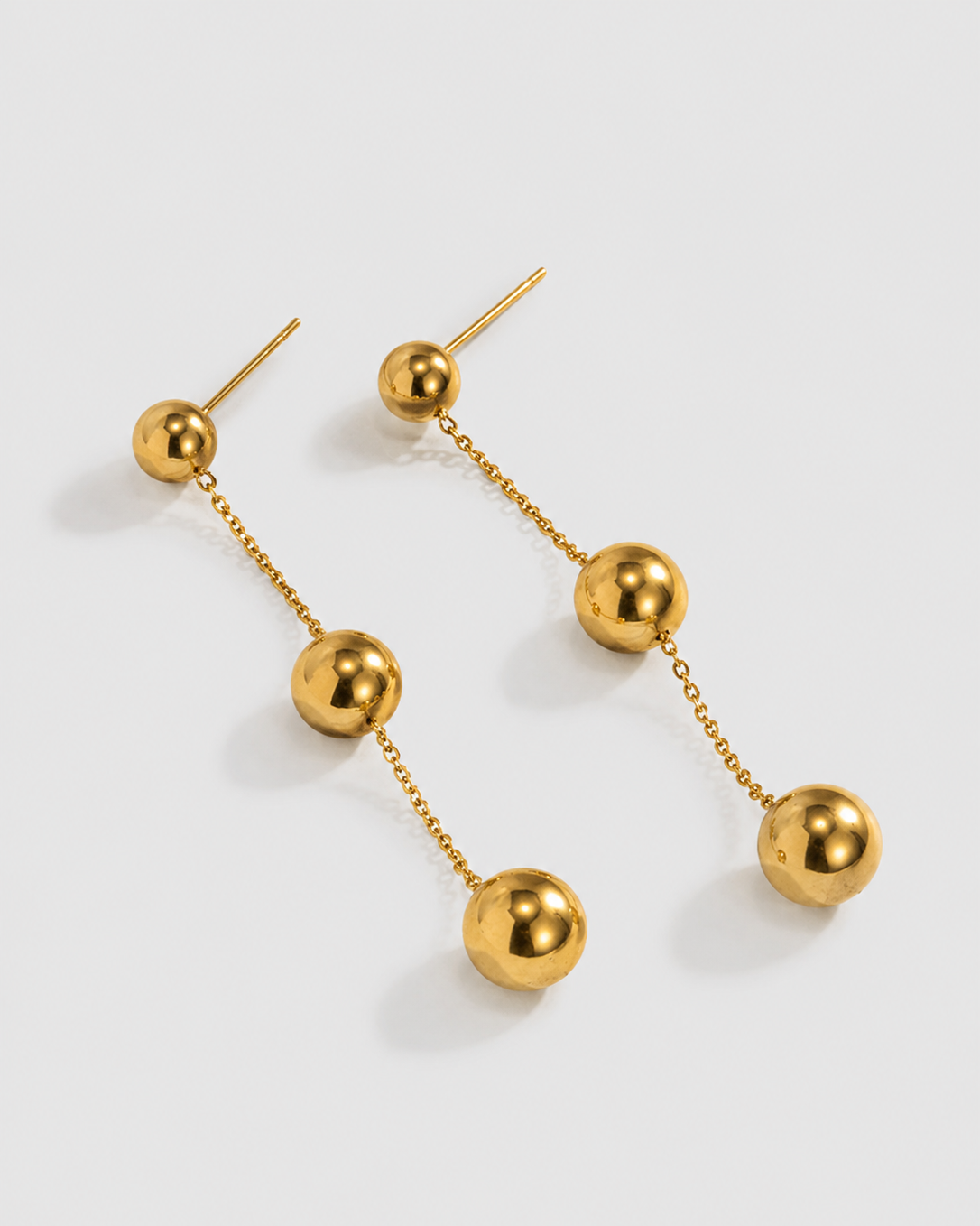 A pair of gold dangle earrings with spherical beads connected by delicate chains, displayed on a light gray background.