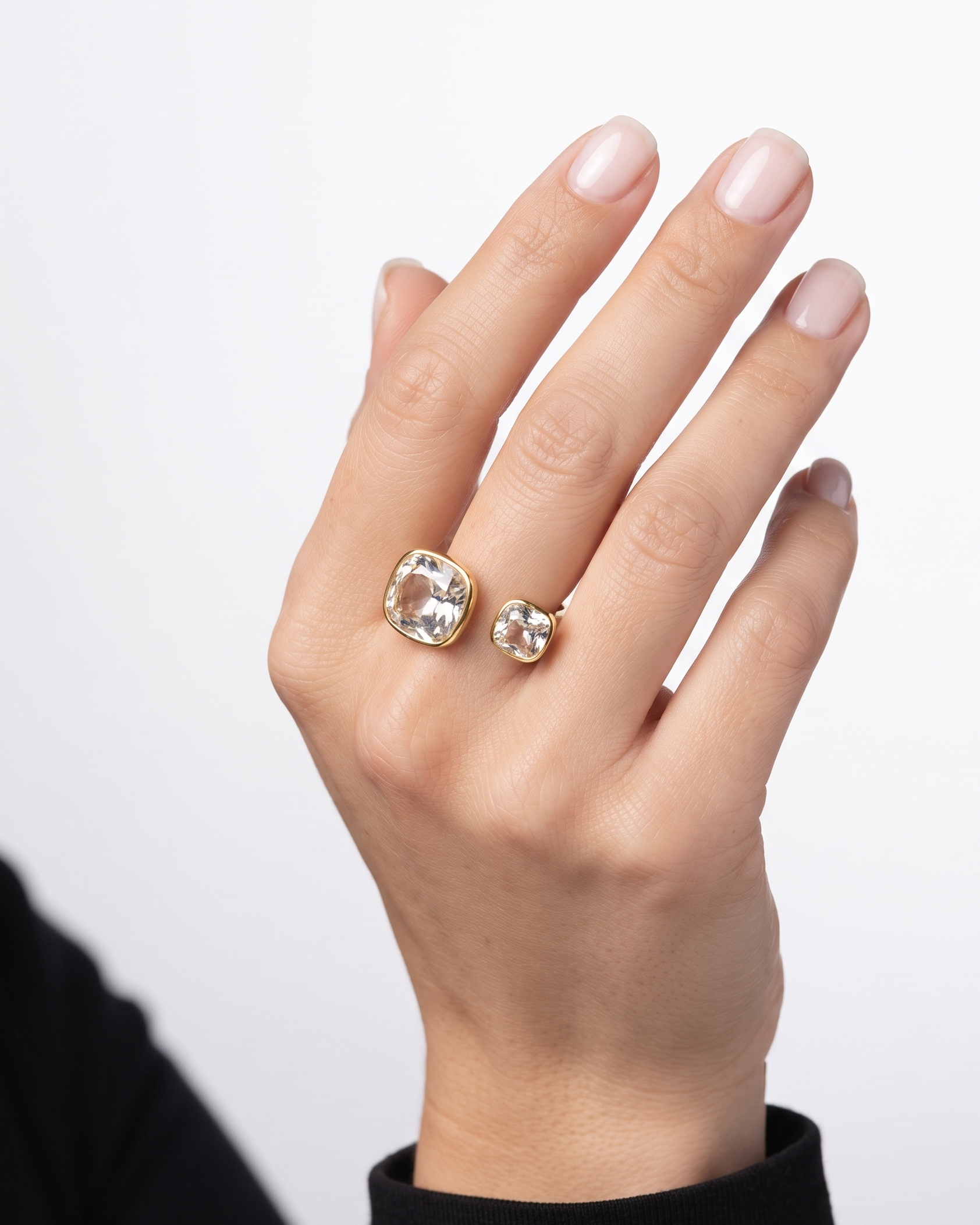 A close-up of a hand wearing two silver rings with clear gemstones, set against a plain light gray background.