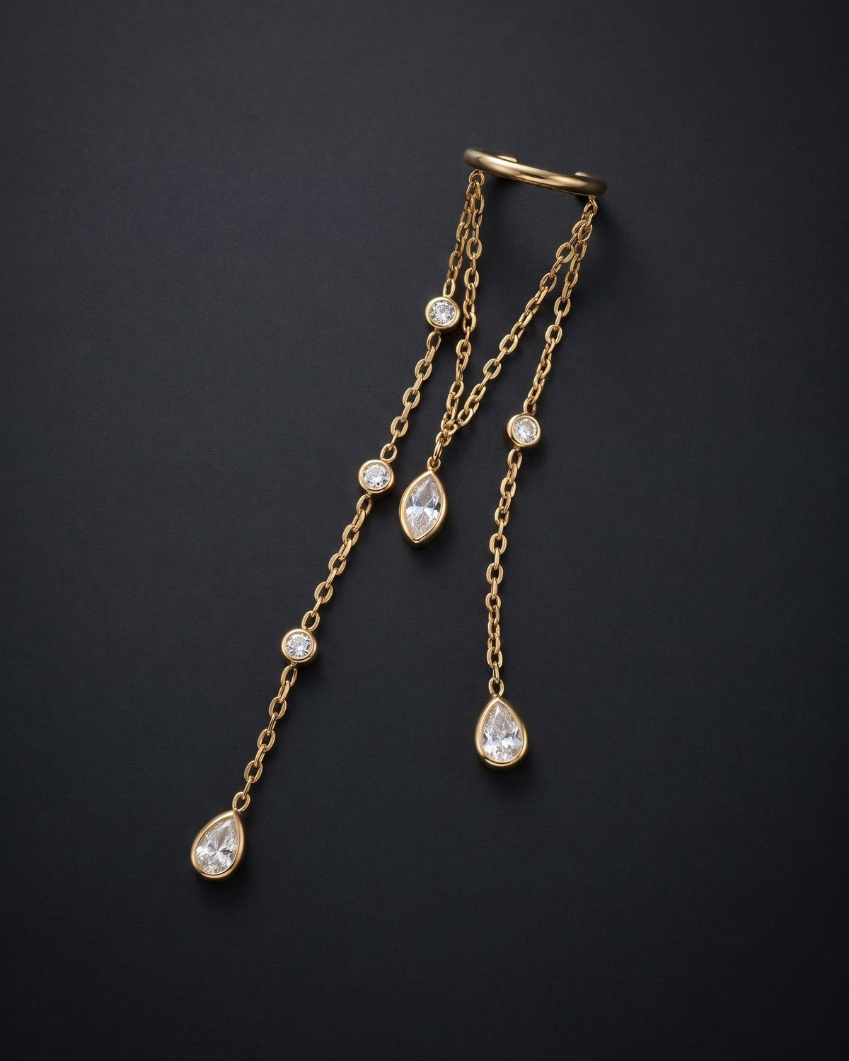 A gold chain body jewelry piece with three dangling chains, each featuring a teardrop-shaped clear gemstone and several small round clear gemstones, displayed on a dark background.
