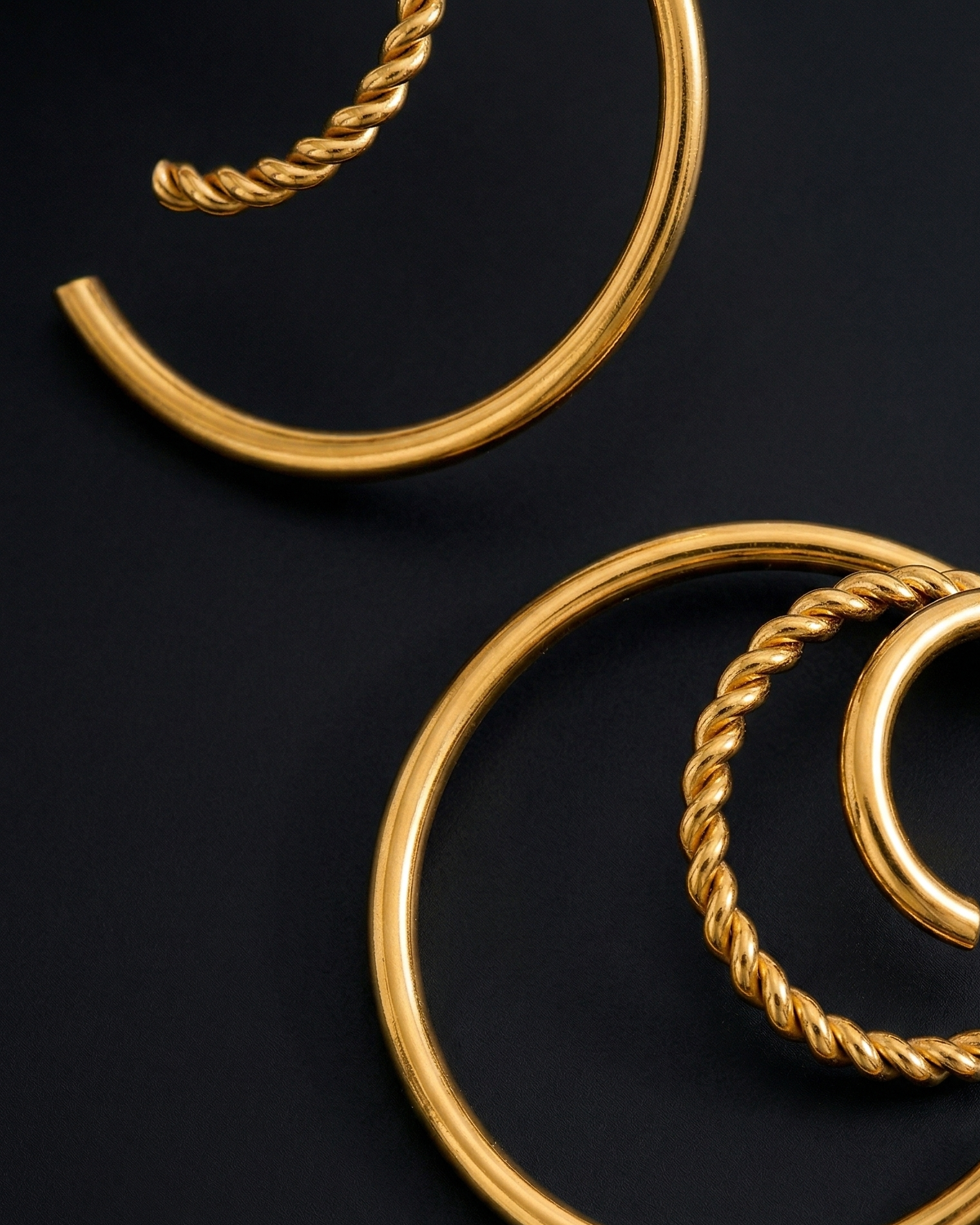 Gold hoop earrings with twisted design on a black background