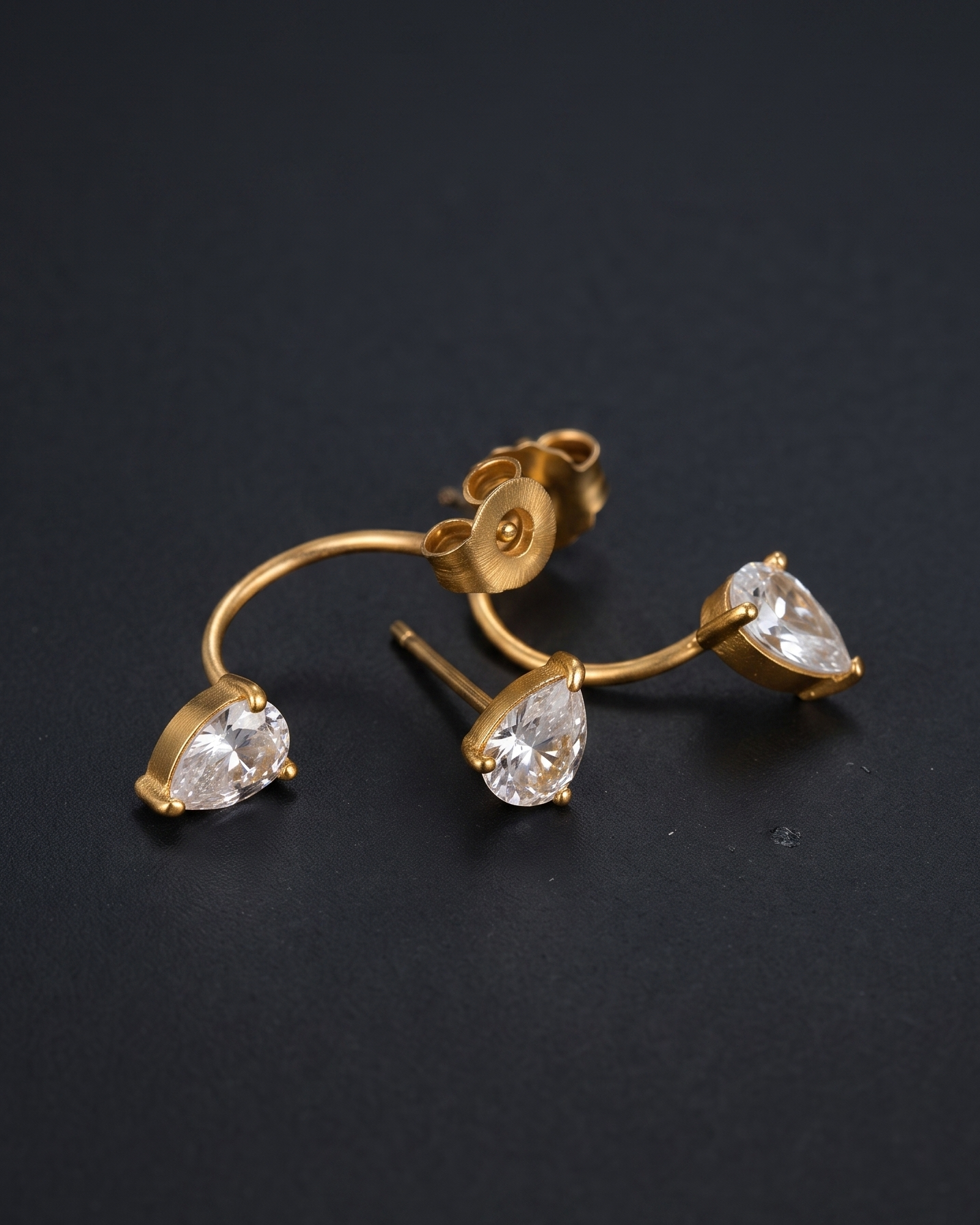 Gold crescent-shaped hoop earrings with three clear teardrop-cut gemstones, displayed on a dark black background.