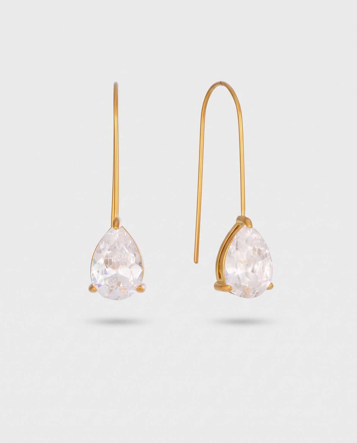A pair of gold drop earrings with pear-cut clear gemstones, shown against a light gray background.