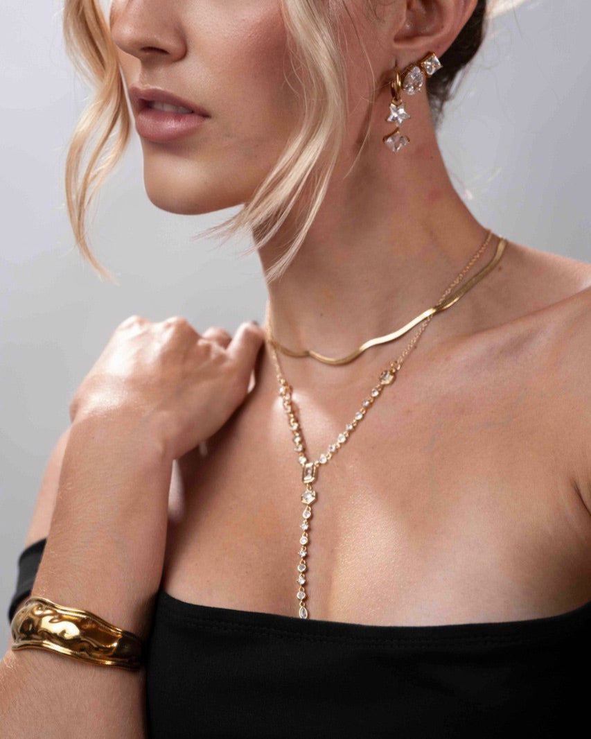 Woman wearing a gold necklace and bracelet with a plain background