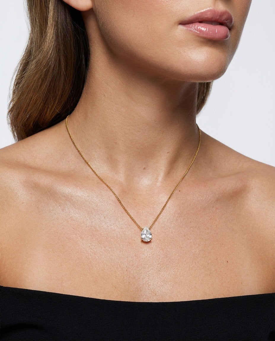 Close-up of a person wearing a gold necklace with a clear pendant on a plain background