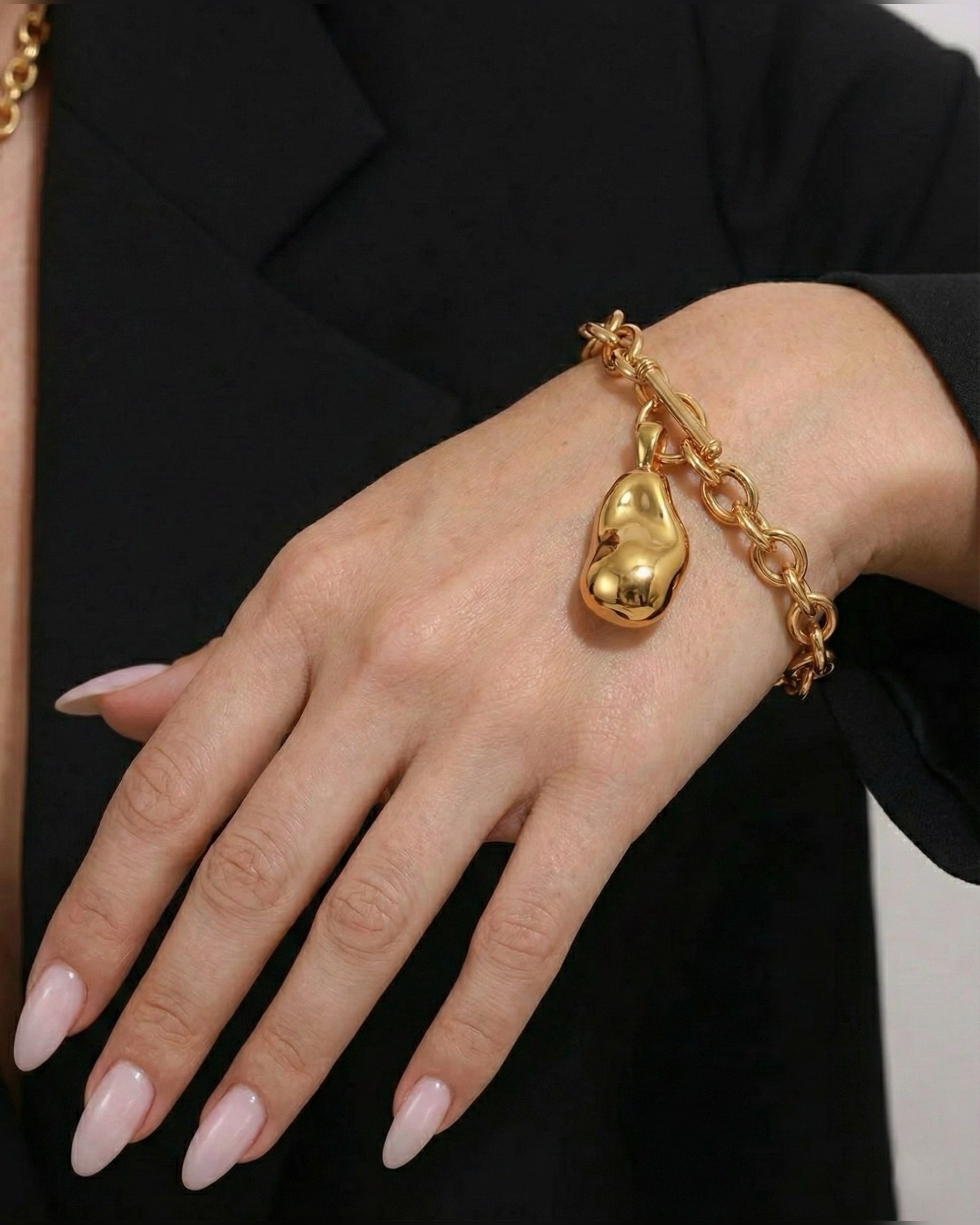 Gold bracelet with a heart-shaped charm on a hand against a black background