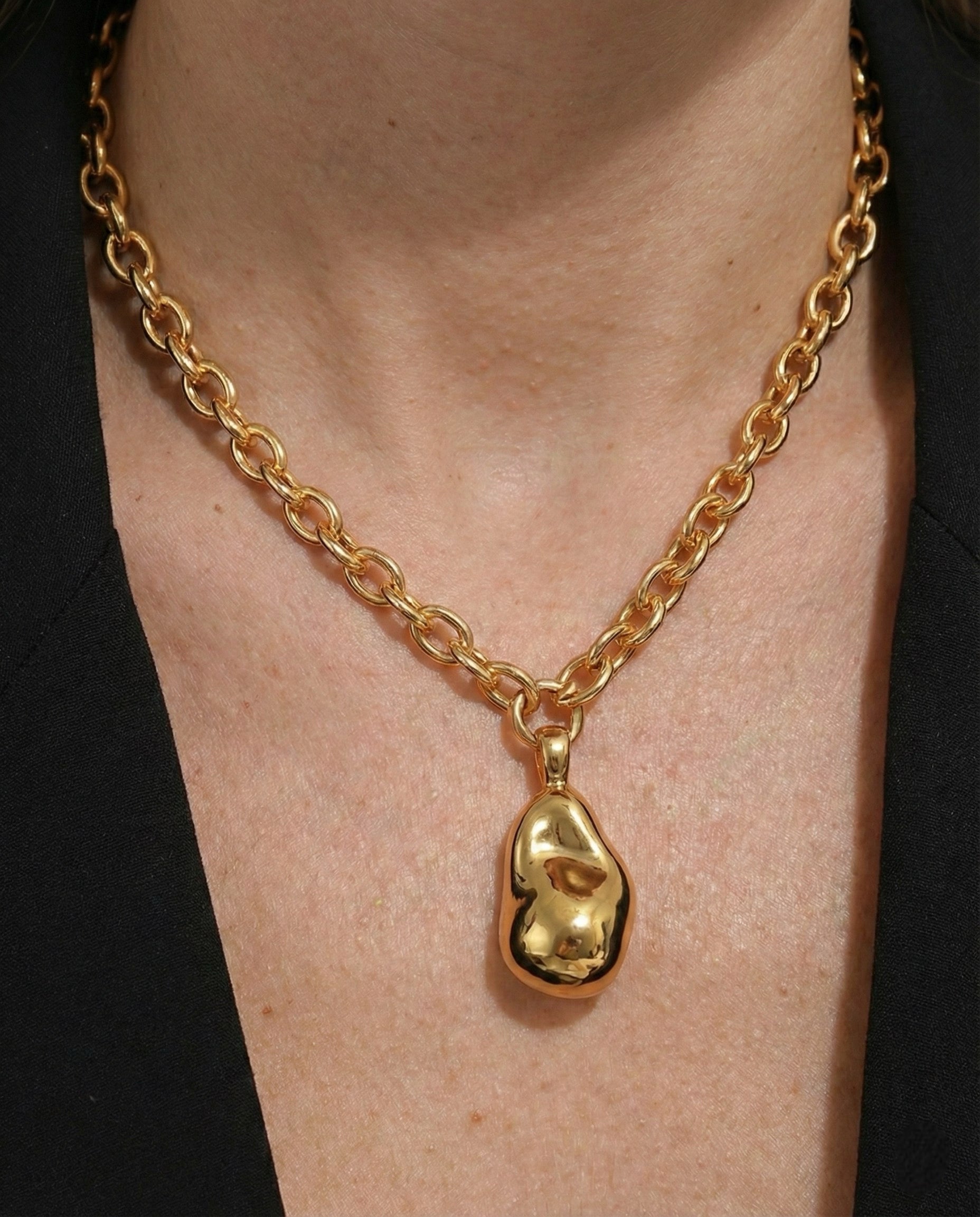 Gold chain necklace with a unique pendant on a person wearing a black garment.