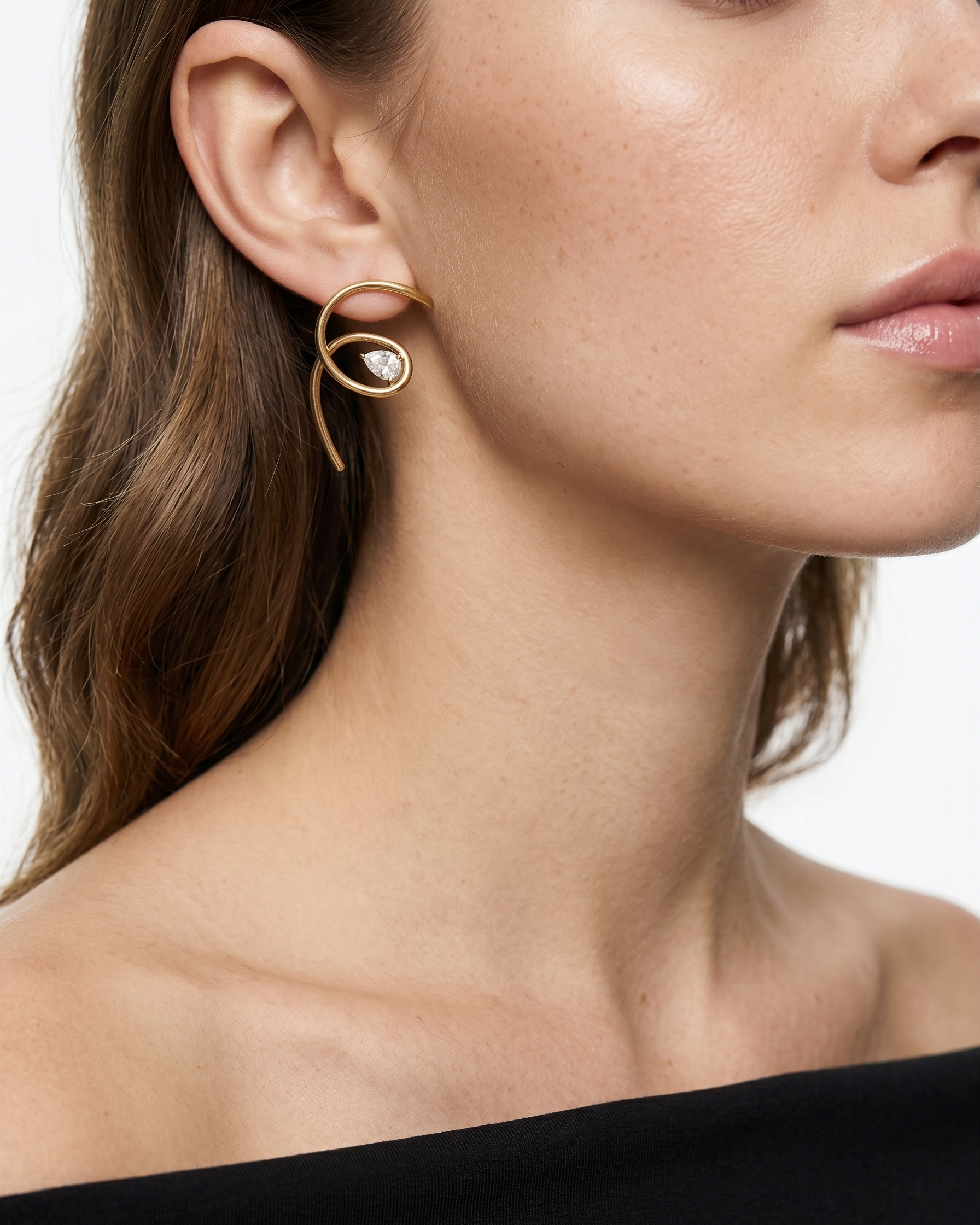 Close-up of a woman wearing a gold hoop earring with a clear gemstone.