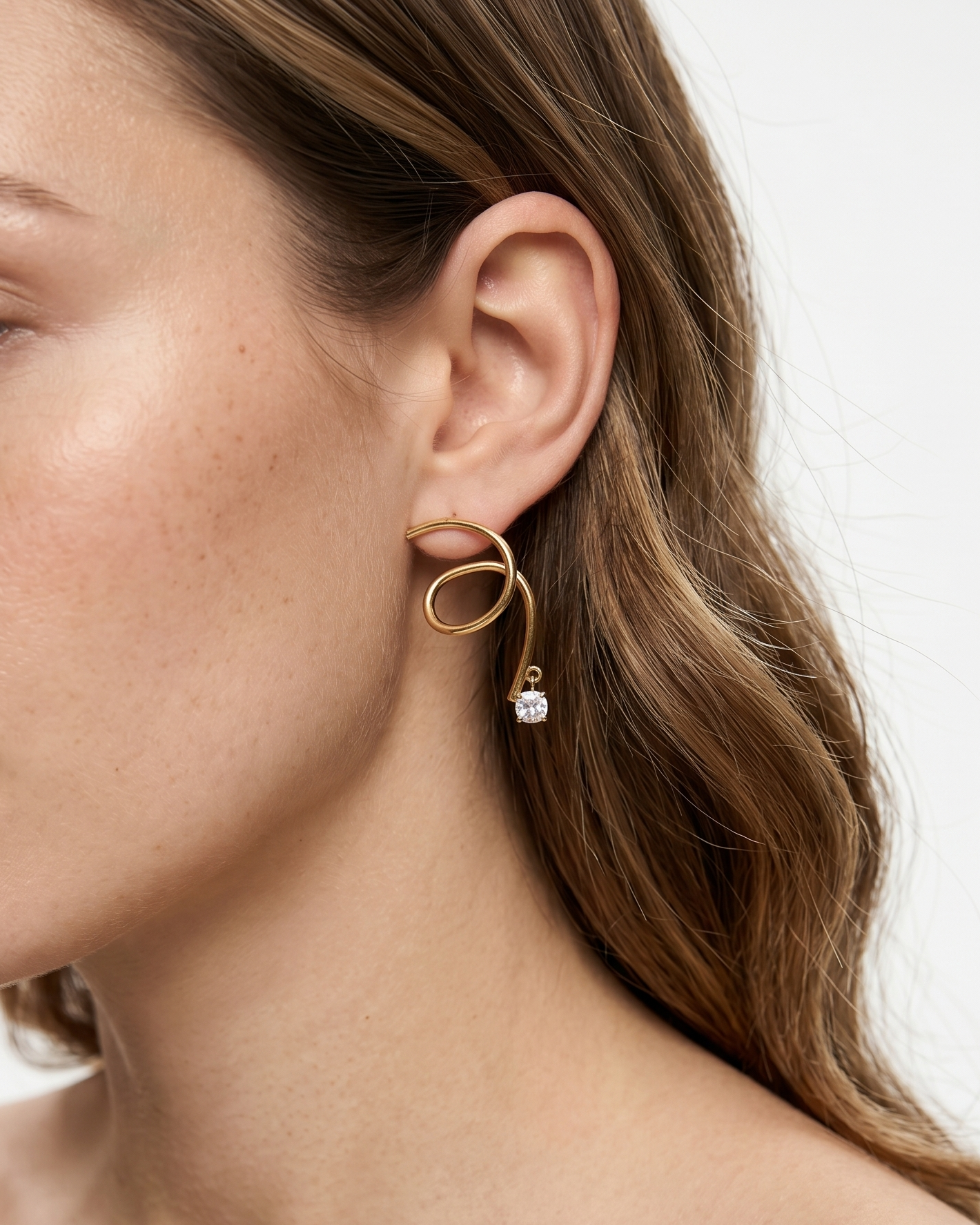 Close-up of a woman wearing gold earrings with a white gemstone on a neutral background