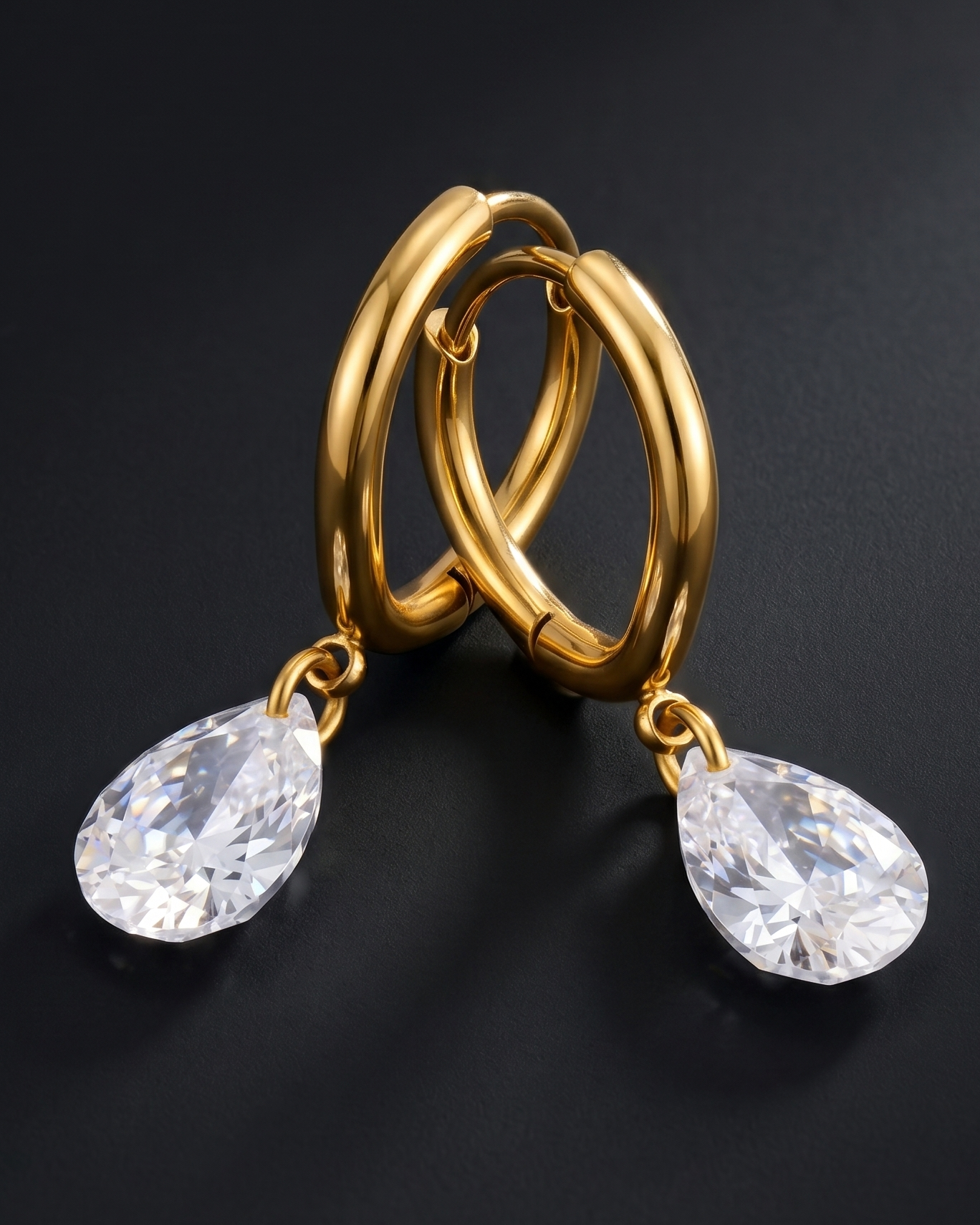Gold hoop earrings with teardrop-shaped crystals on a dark background