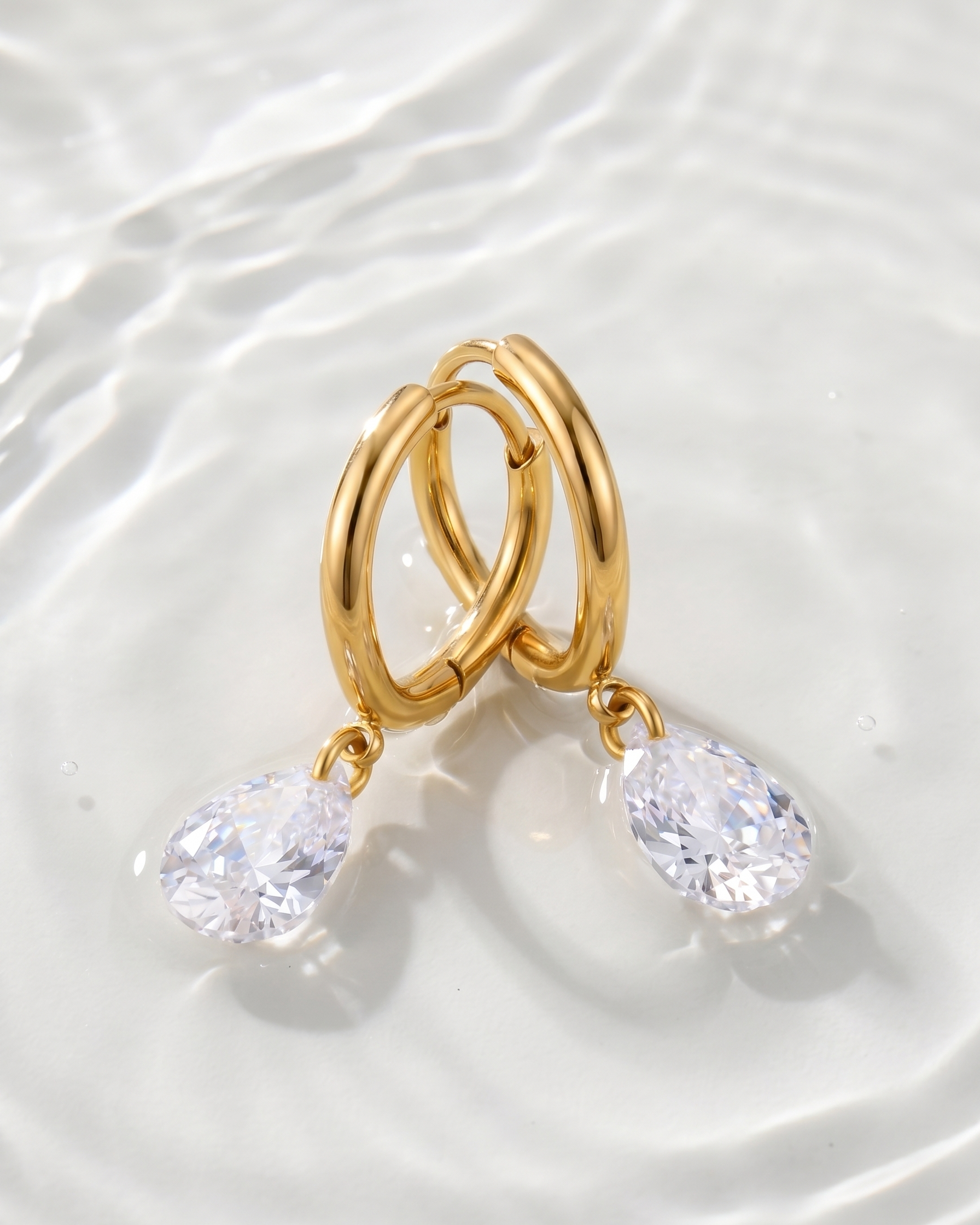 Gold hoop earrings with crystal drops on a white fabric background