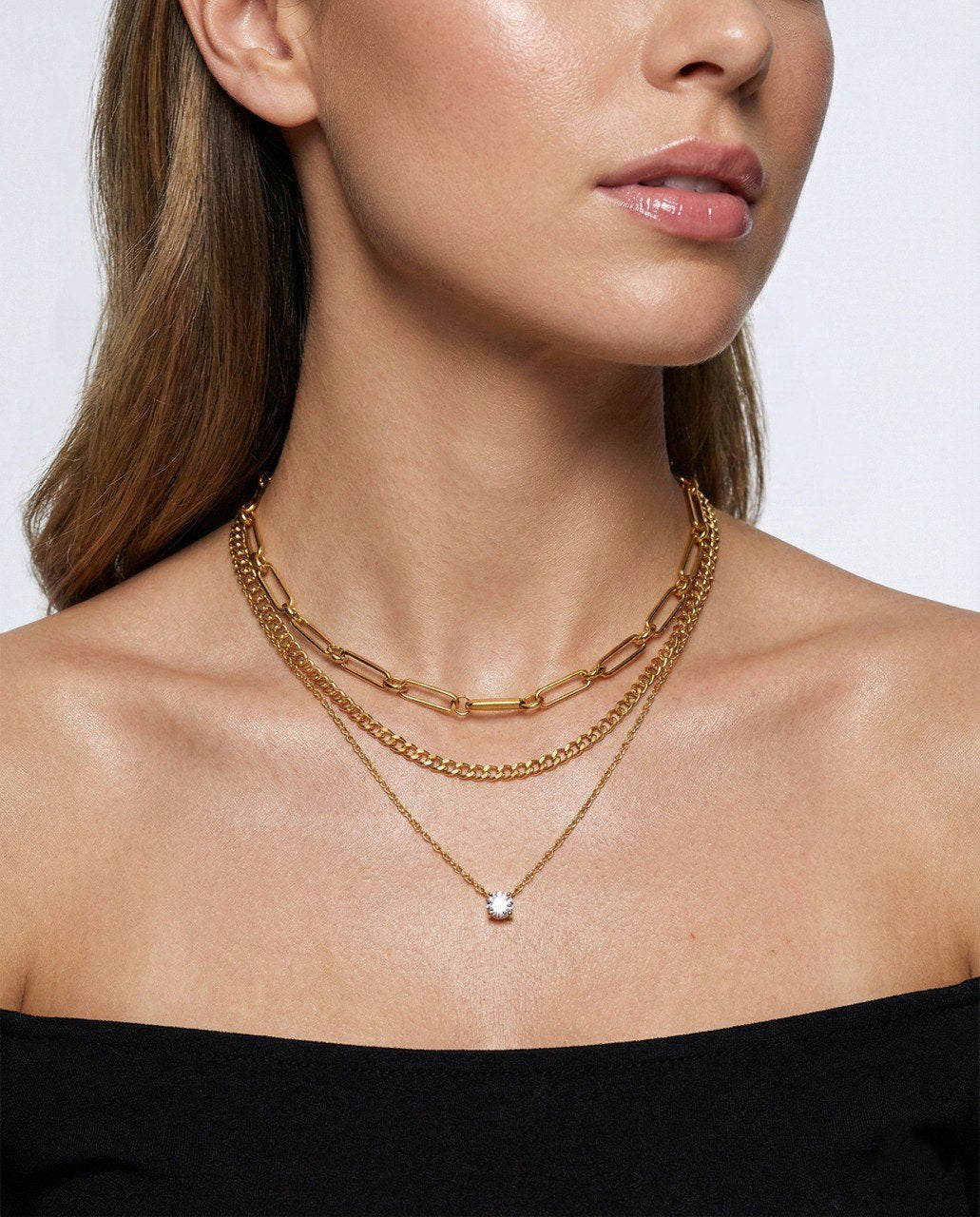 Close-up of a woman wearing two gold necklaces against a neutral background