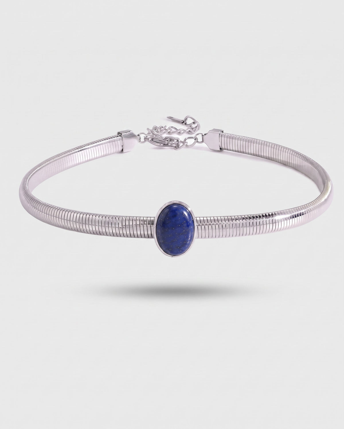 A silver-toned snake-style bangle bracelet featuring a central oval blue lapis lazuli stone, shown against a light gray background.