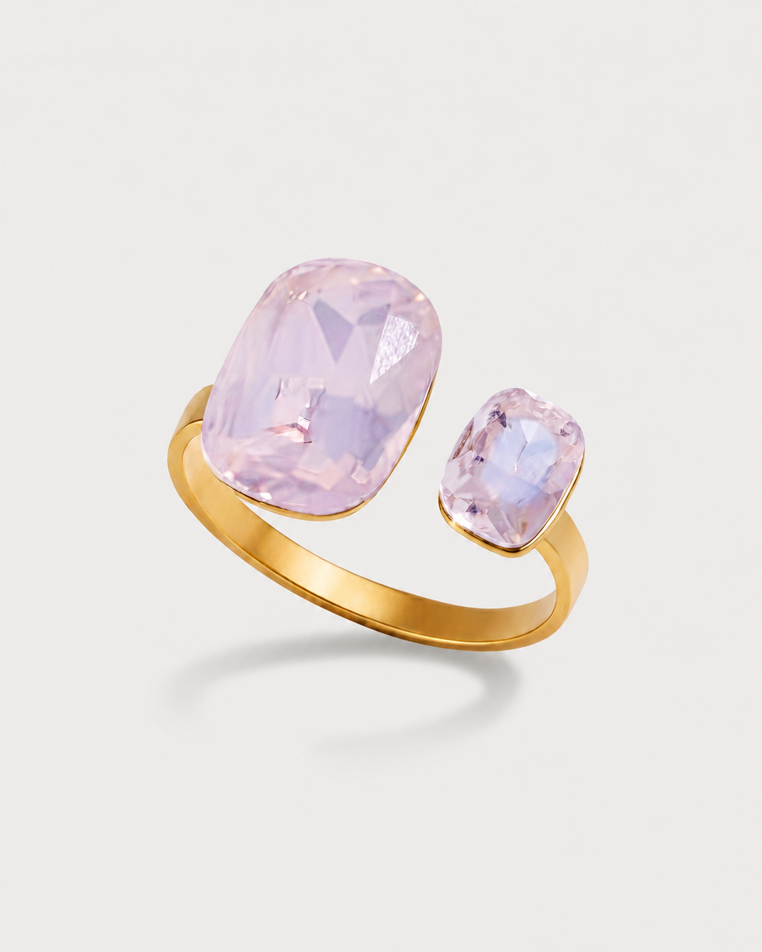 A gold ring featuring two light pink cushion-cut gemstones, one larger and one smaller, set in a minimalist gold band on a light gray background.