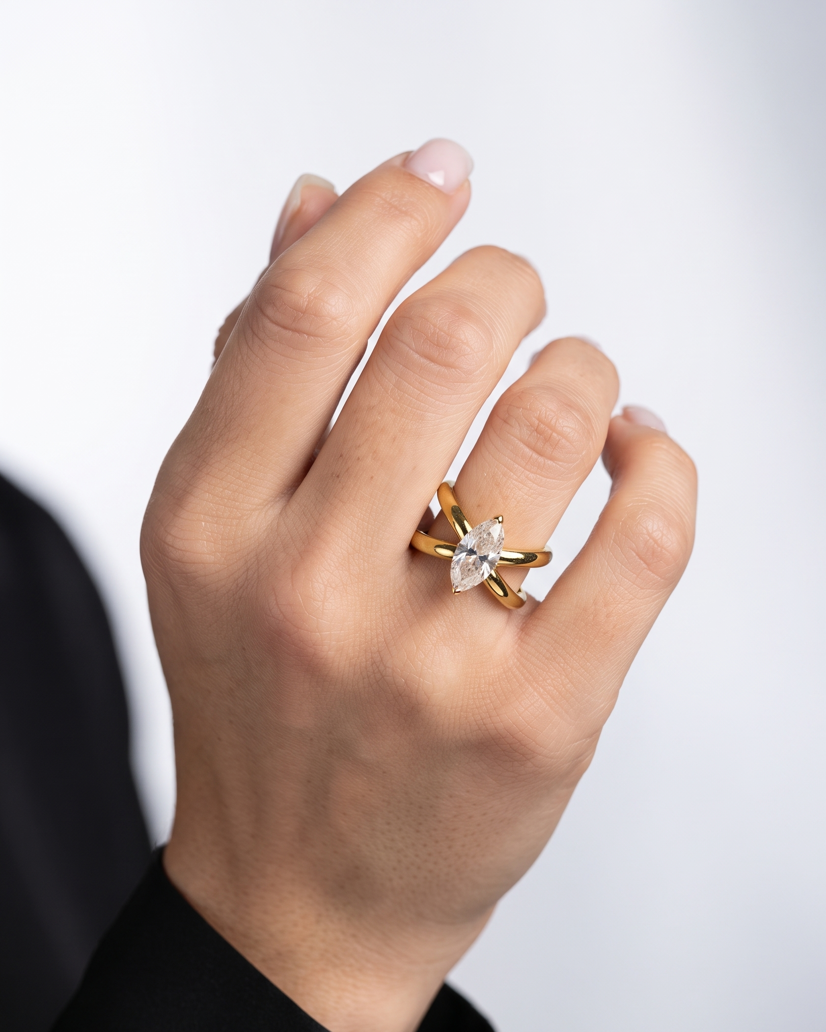 A close-up of a hand wearing a gold ring with a marquise-cut clear gemstone, set against a clean light gray background.