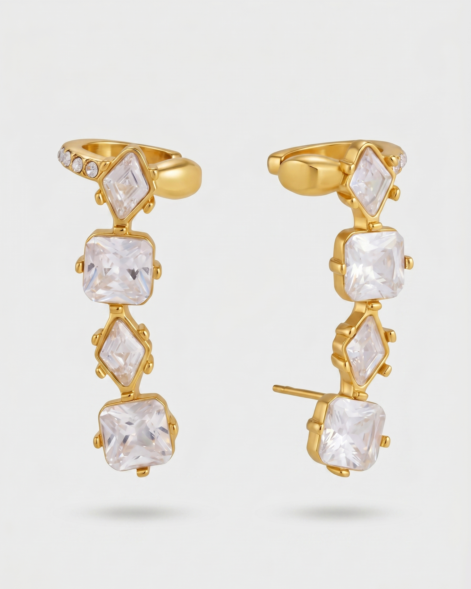 Gold earrings with clear gemstones on a light gray background