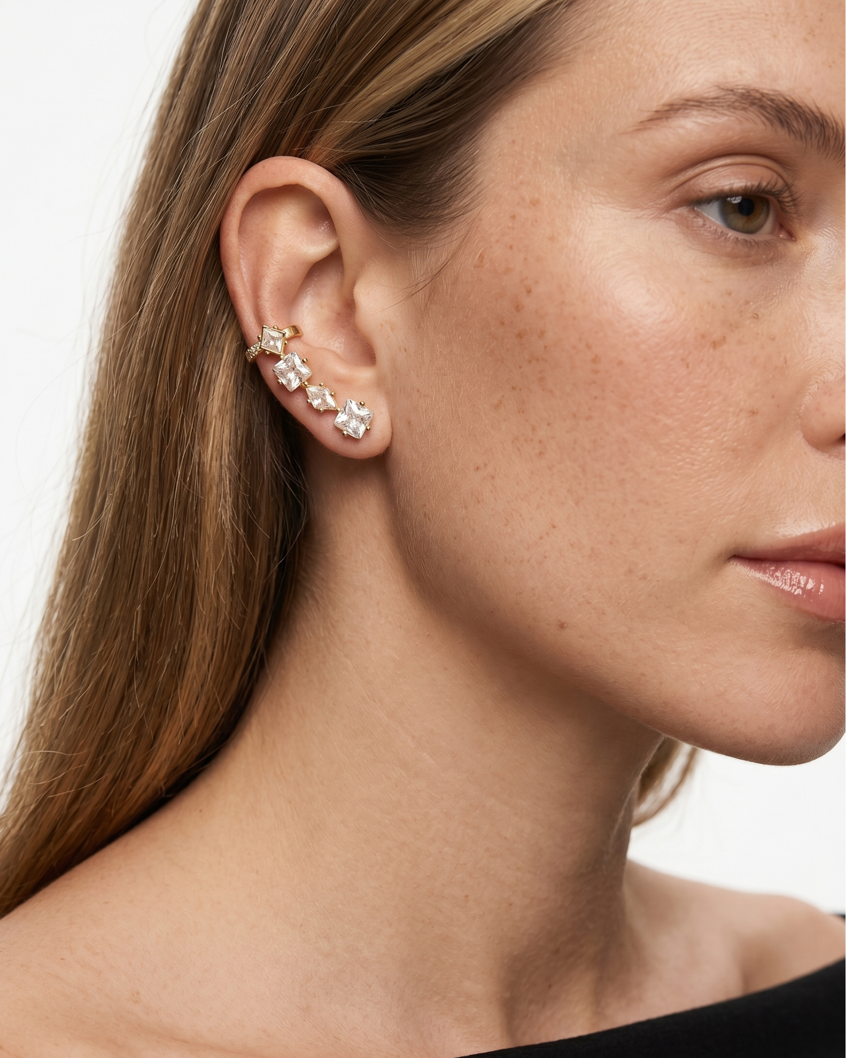Close-up of a woman wearing gold earrings with small stones on a plain background