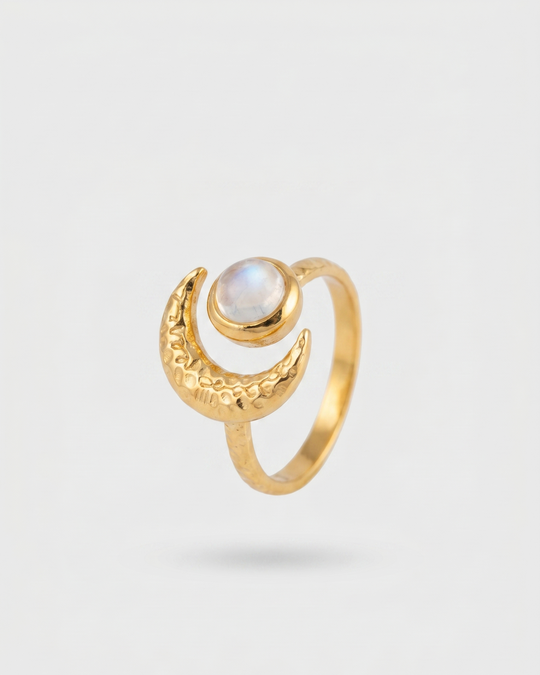 Gold ring with a moon design and central gemstone on a light gray background
