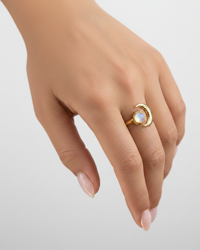 Gold ring with a moonstone on a hand against a light gray background