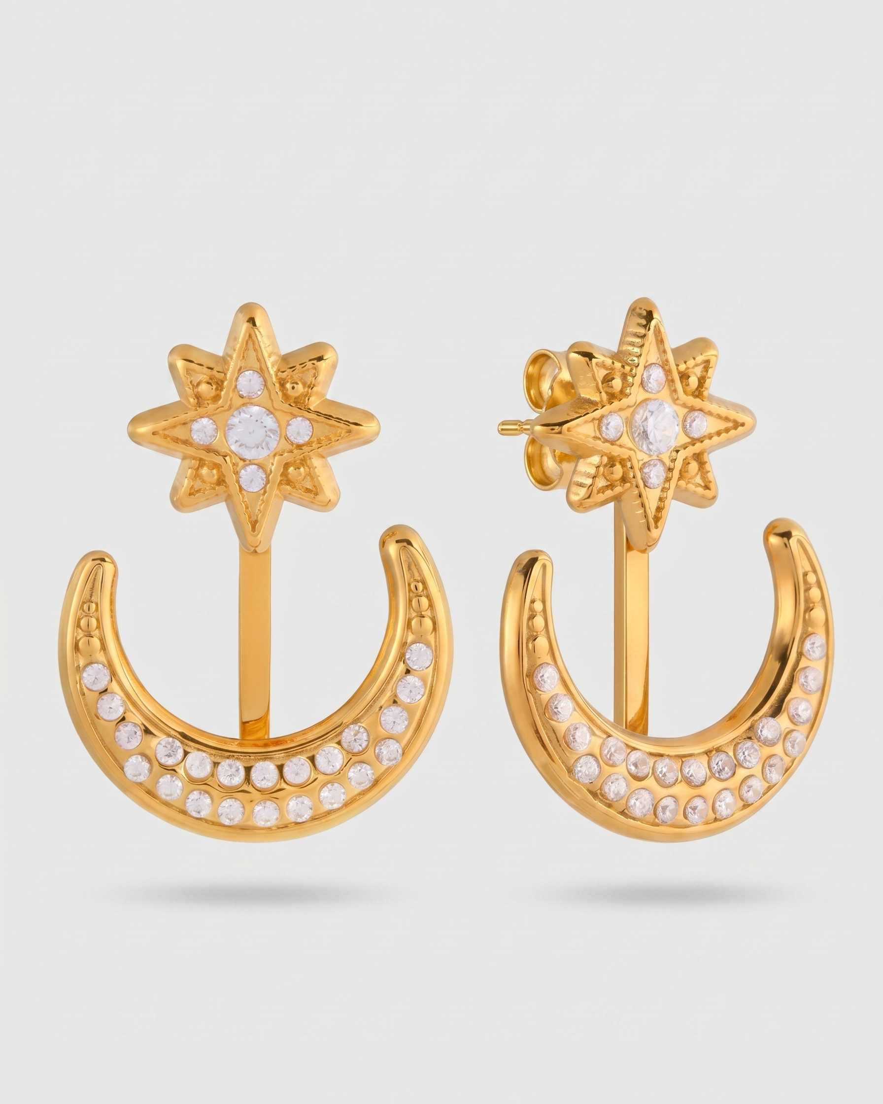 Gold earrings with star and crescent moon design on a light gray background