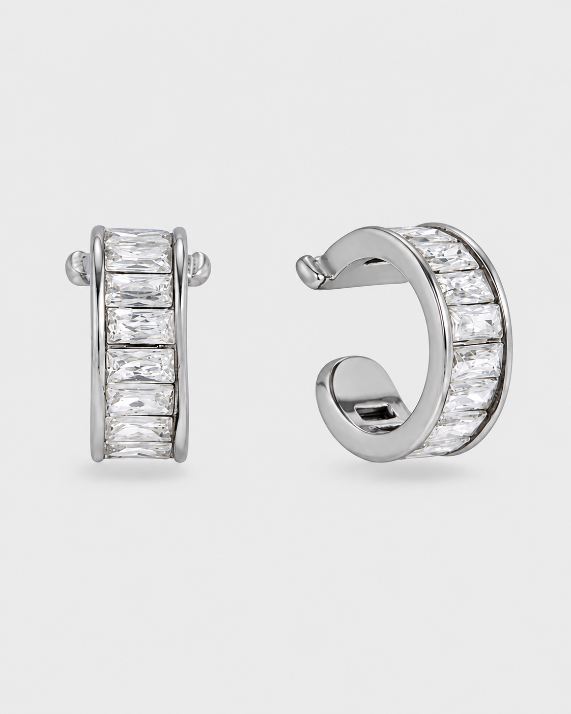 A pair of silver huggie hoop earrings with rectangular clear baguette stones, shown from front and side angles on a light gray background.
