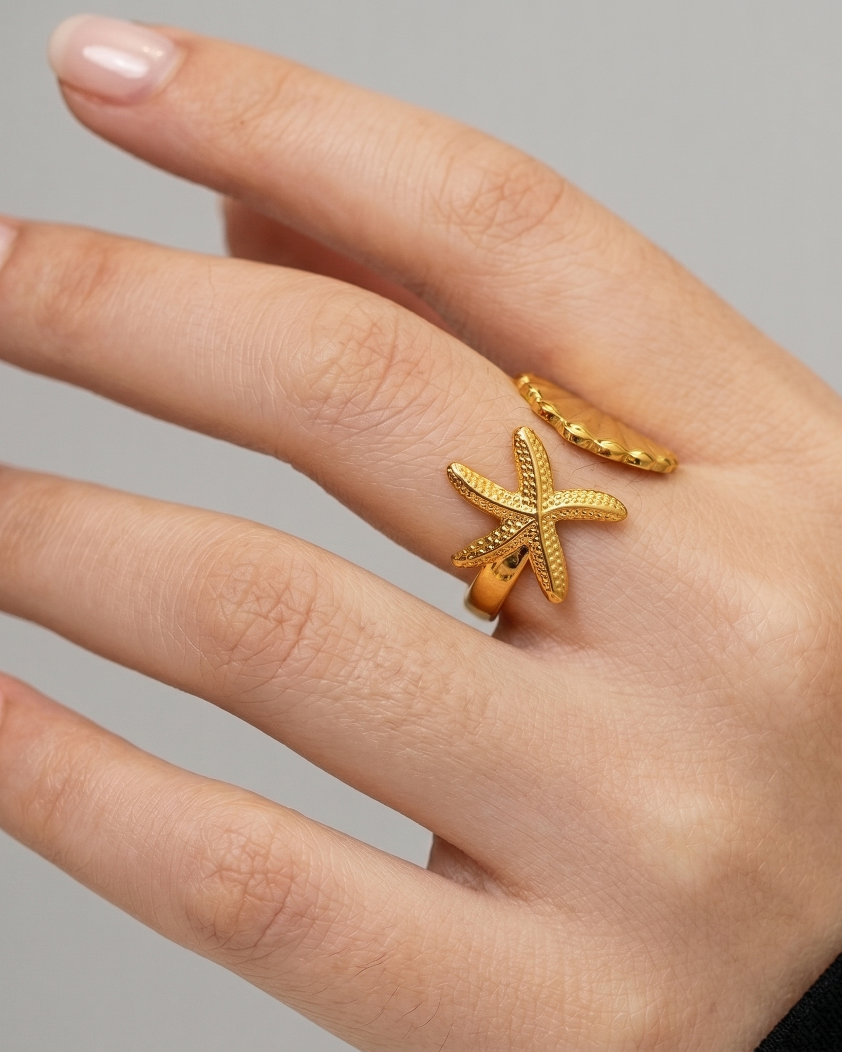 Gold starfish ring on a hand against a neutral background
